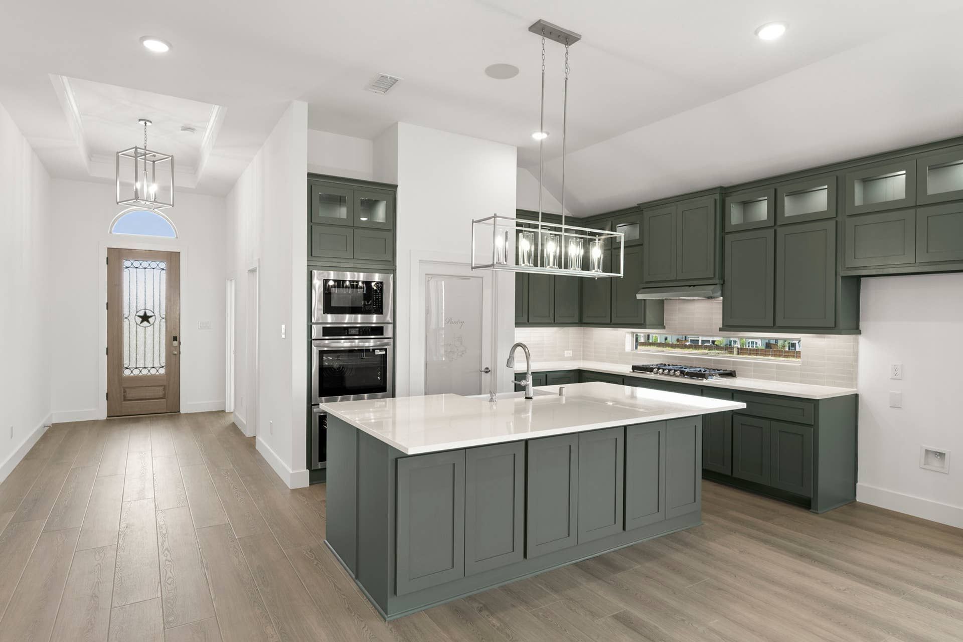 Modern kitchen with green cabinets, large island, and elegant light fixtures.