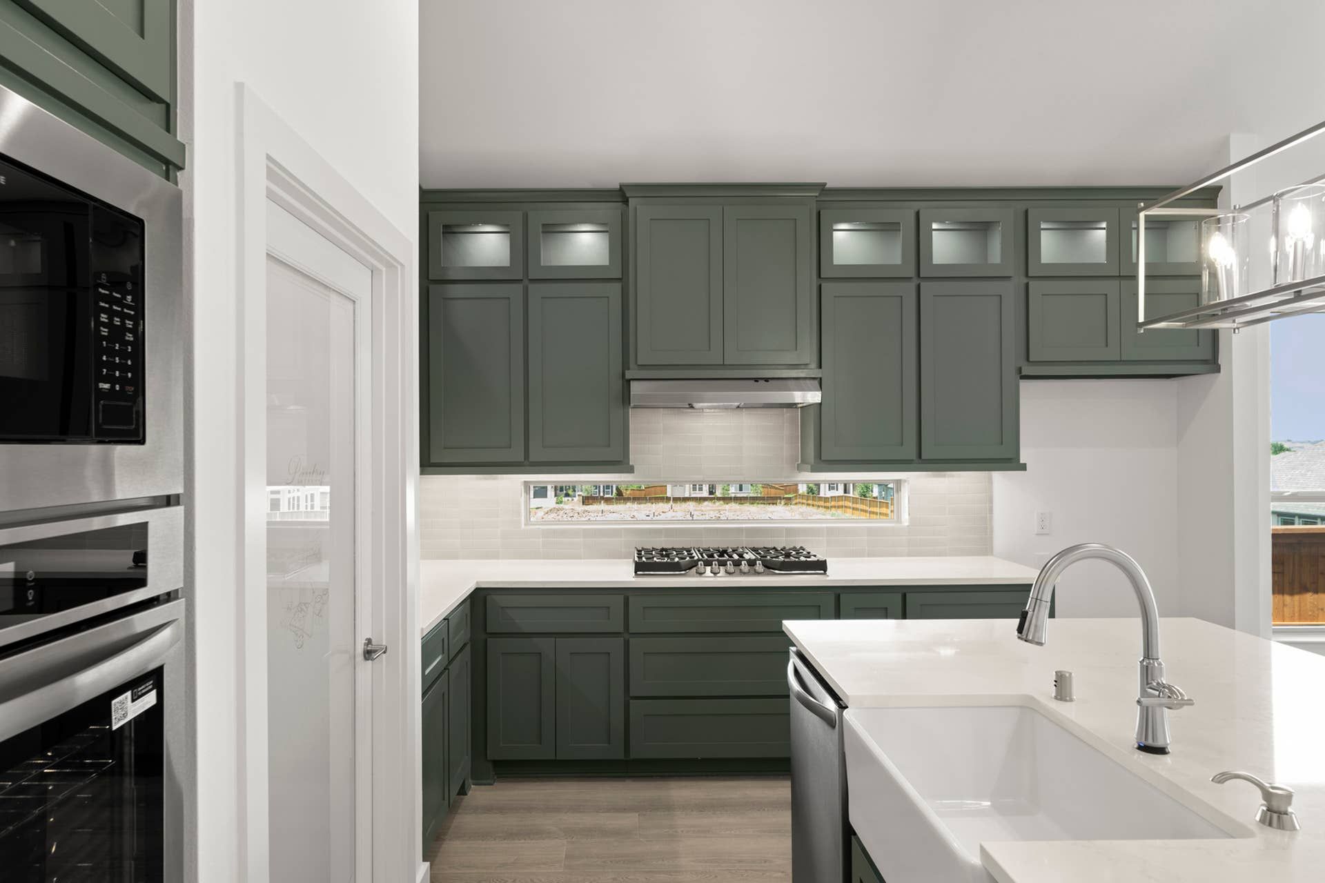 Modern kitchen with dark green cabinets, white countertops, and stainless steel appliances.
