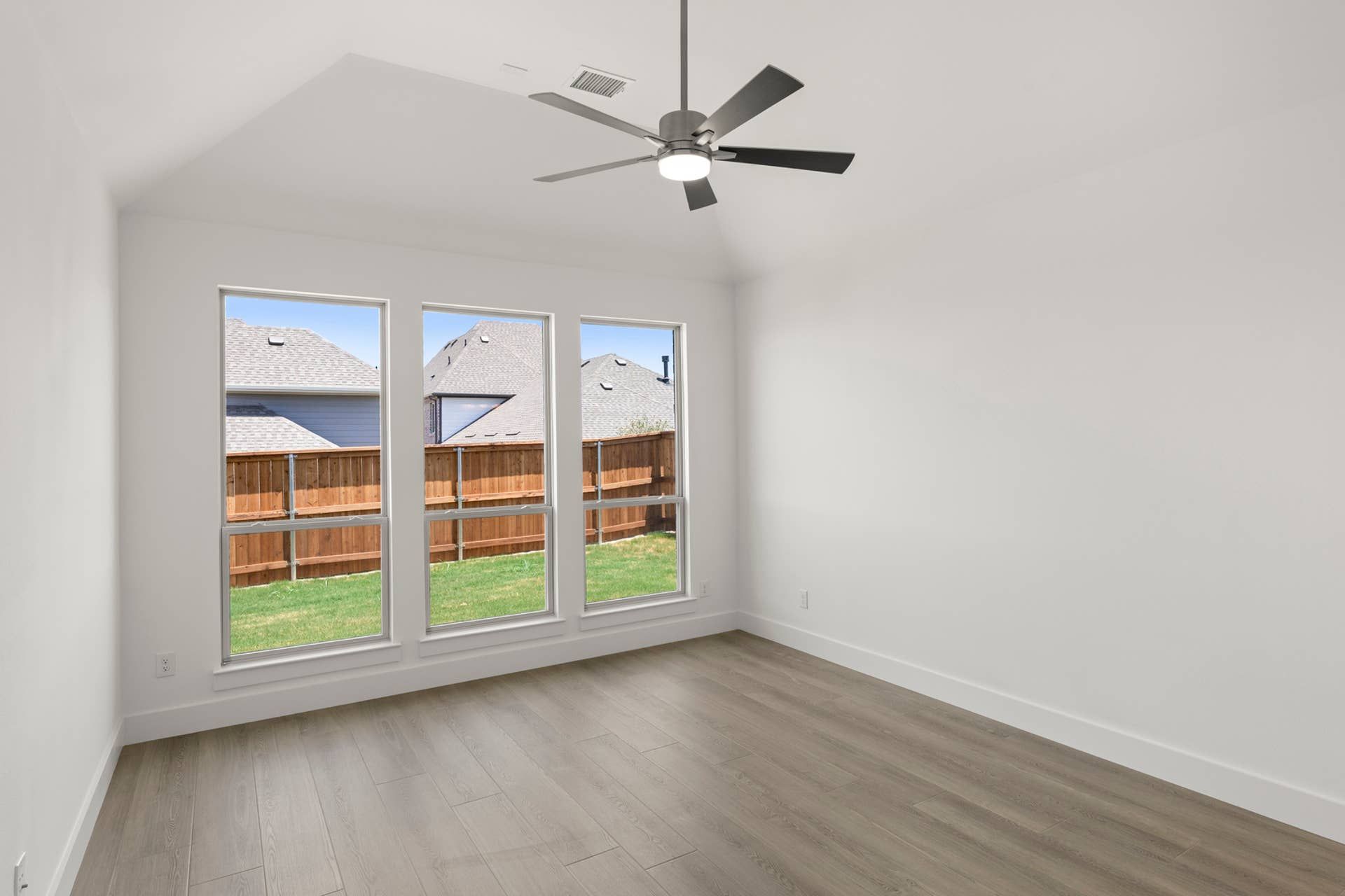 Bright room with large windows, wood flooring, and ceiling fan.