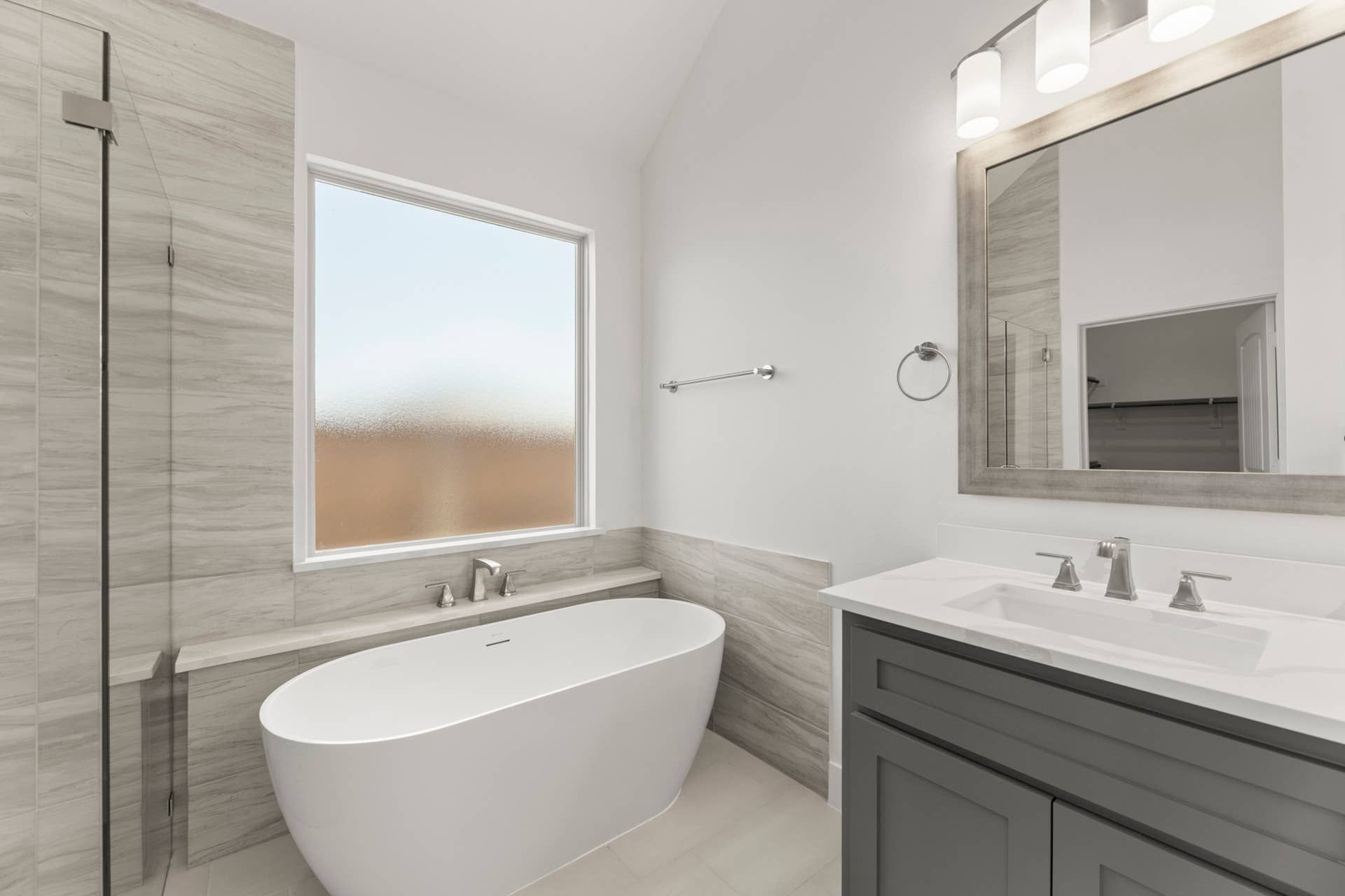 Modern bathroom with freestanding tub, large mirror, and frosted window.