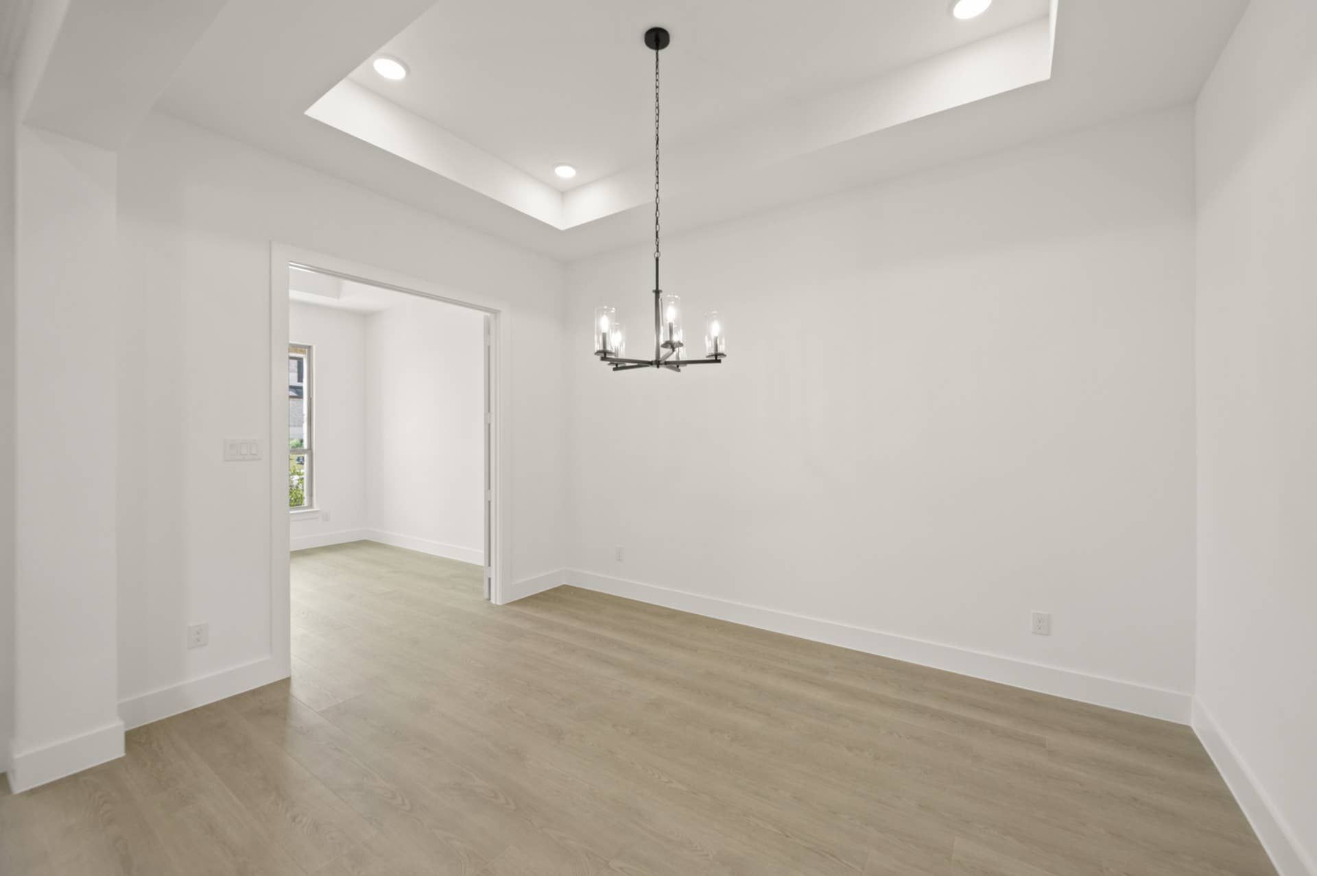 Modern dining room with tray ceiling and elegant chandelier.