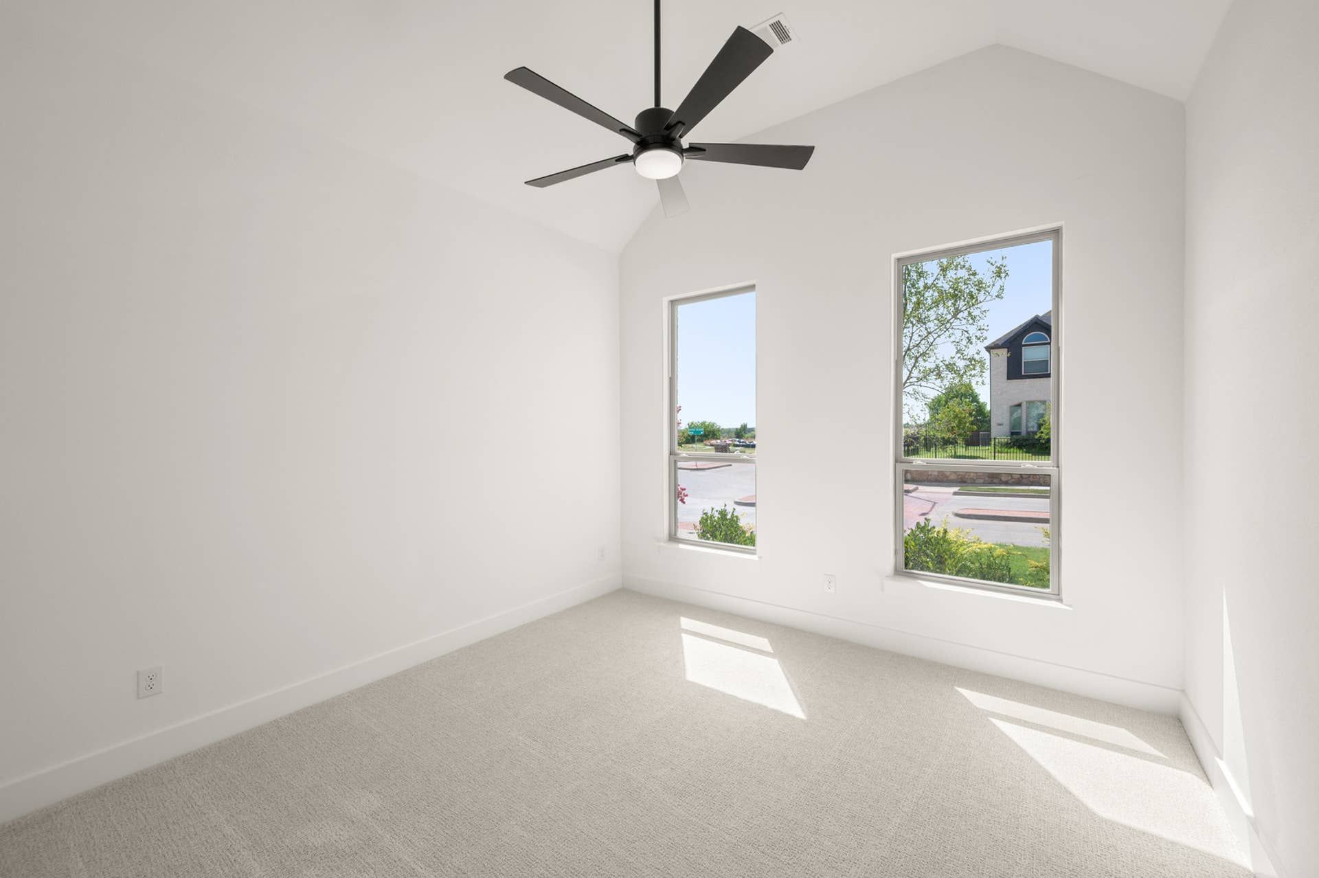 Bright bedroom with vaulted ceiling, ceiling fan, and two large windows.