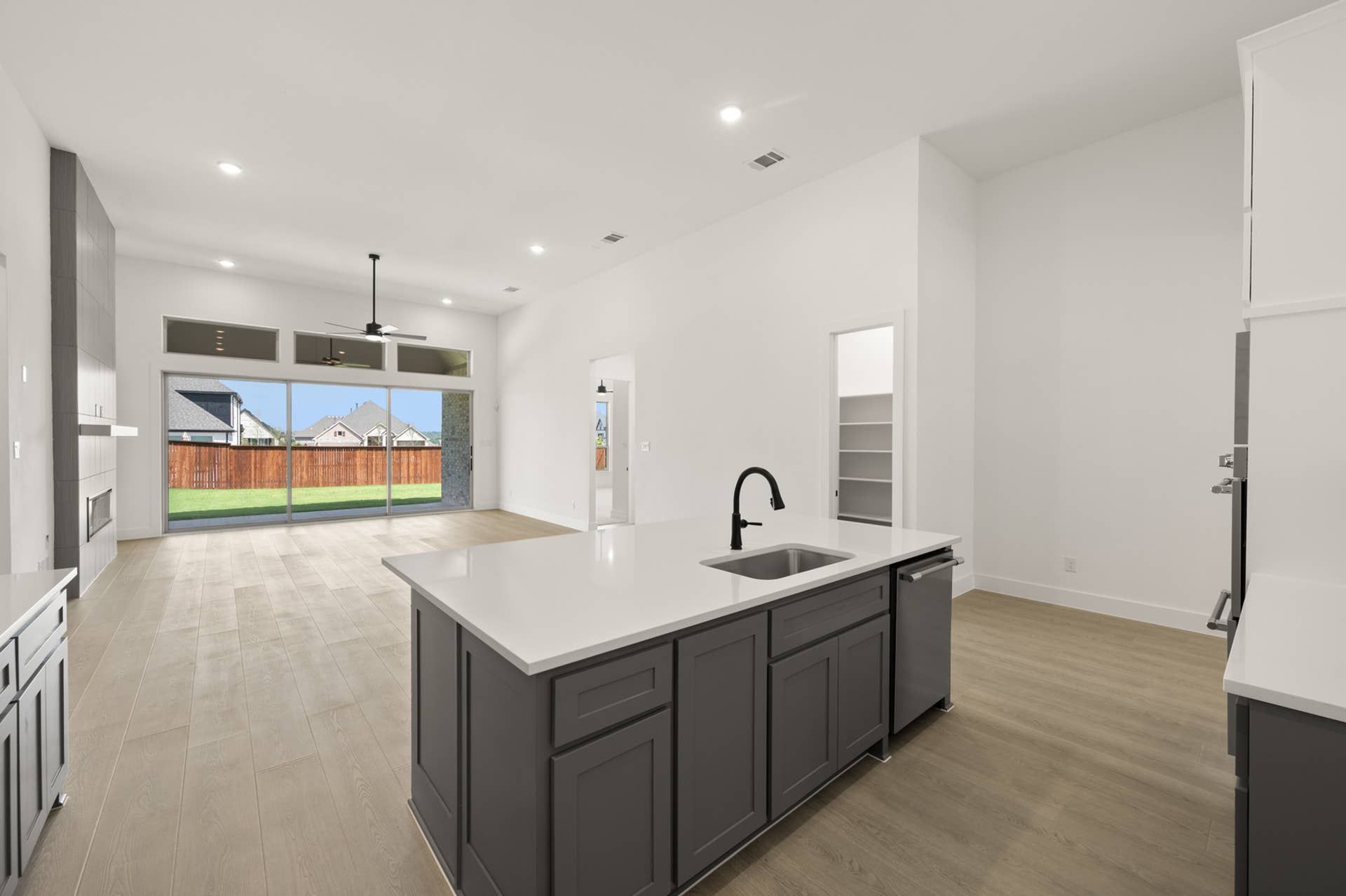 Modern kitchen with island, sleek cabinetry, and large windows overlooking backyard.