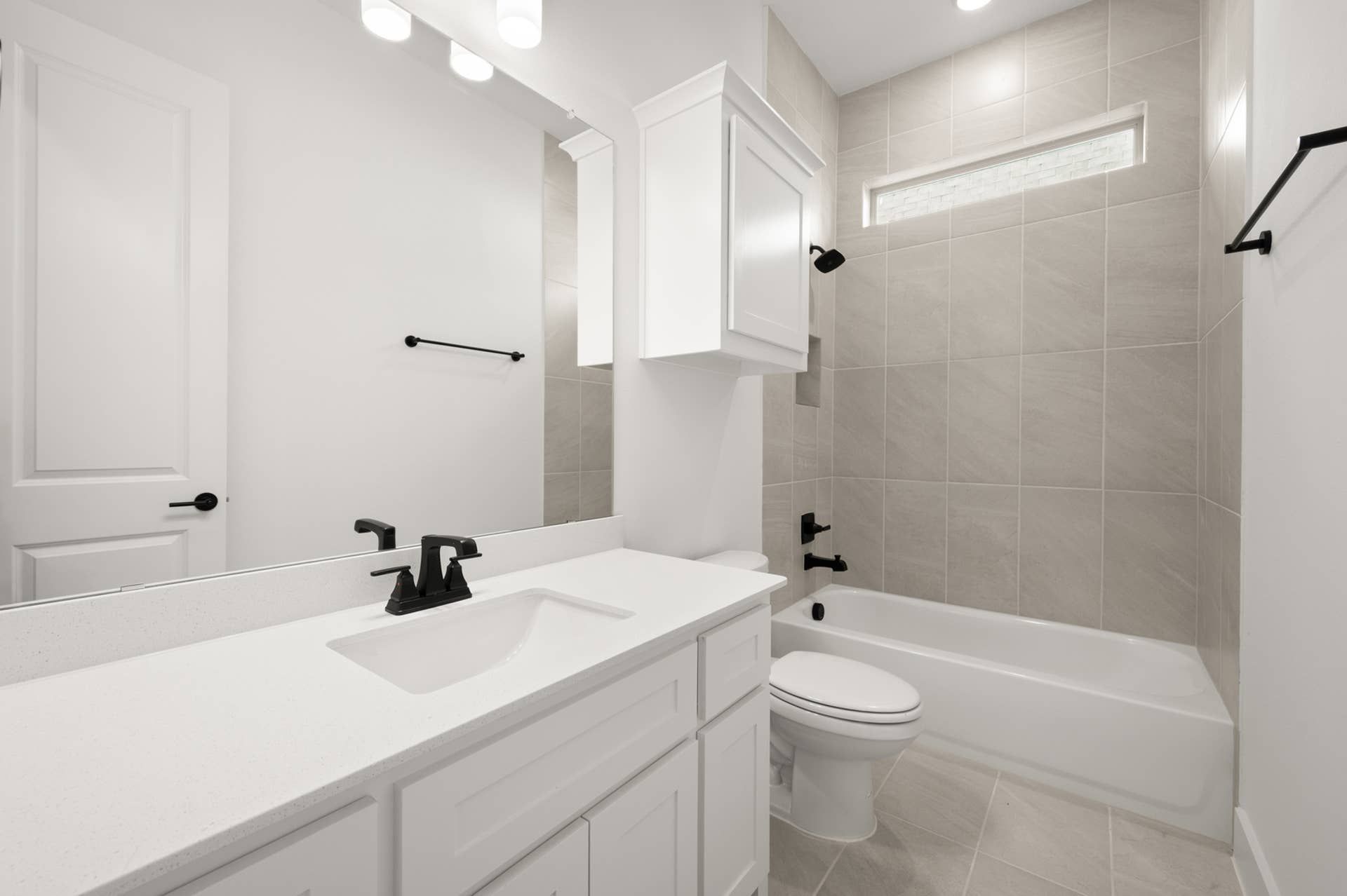 Modern bathroom with white cabinetry, sleek fixtures, and tiled bathtub area.