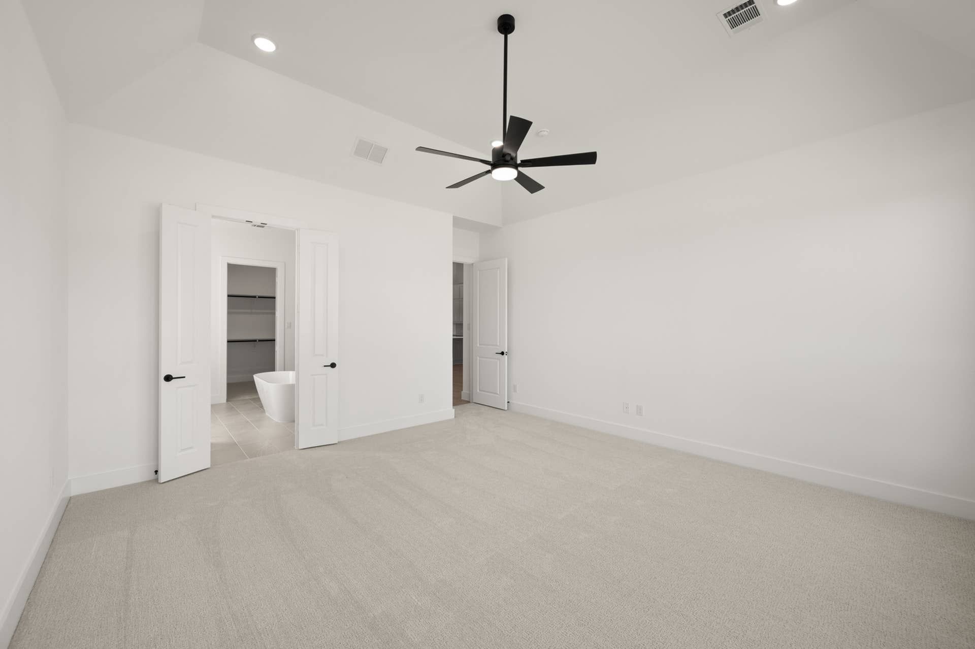 Spacious primary suite with modern ceiling fan and en-suite bathroom view.