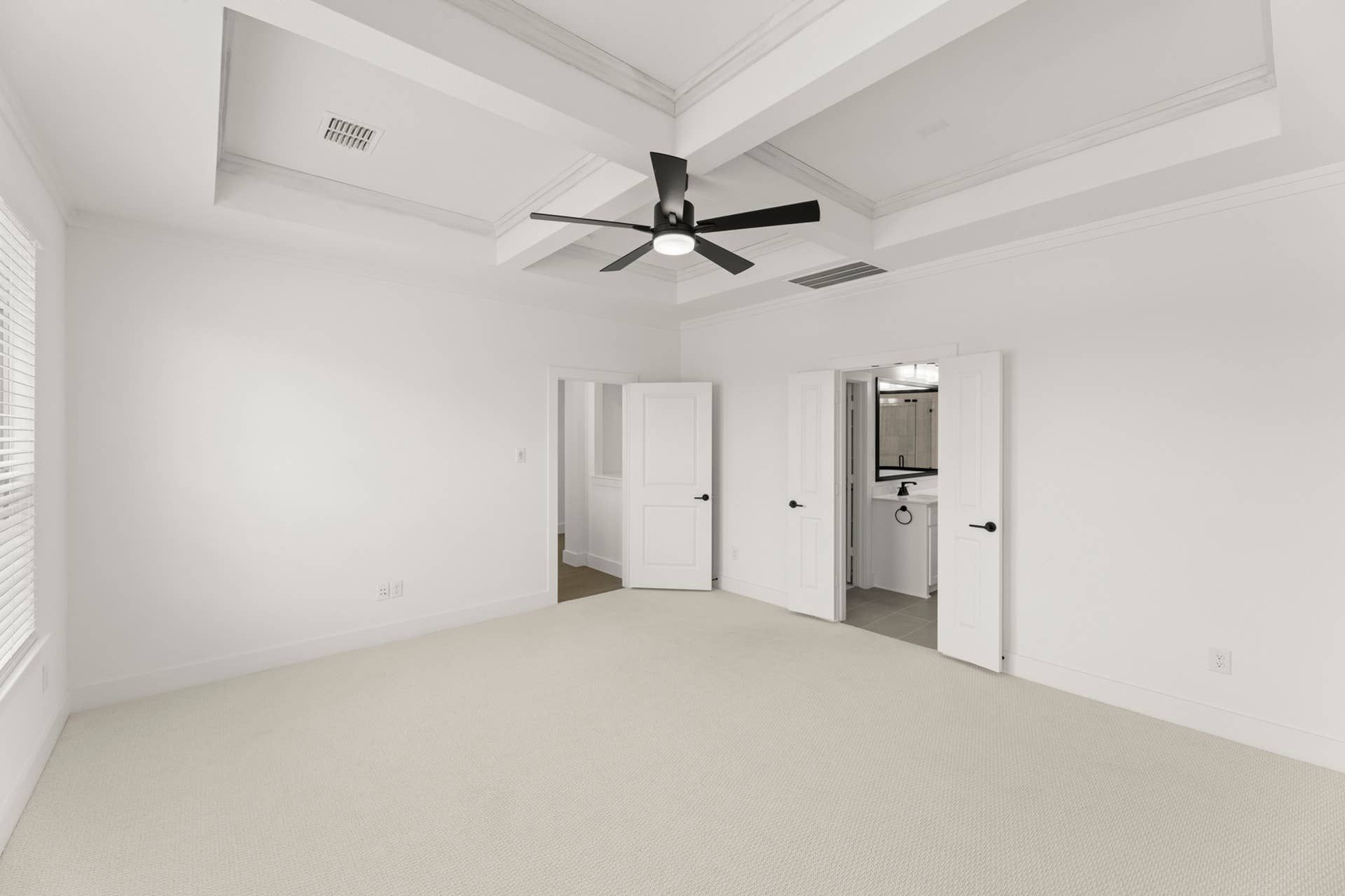 Spacious bedroom with tray ceiling, ceiling fan, and open doors to bathroom.