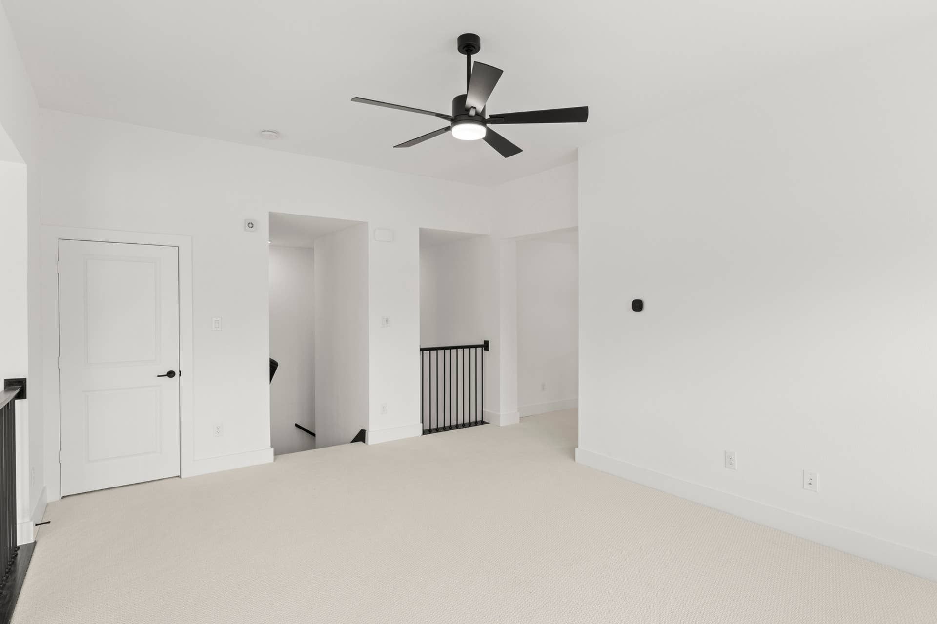 Spacious white-walled room with ceiling fan and carpeted floor.