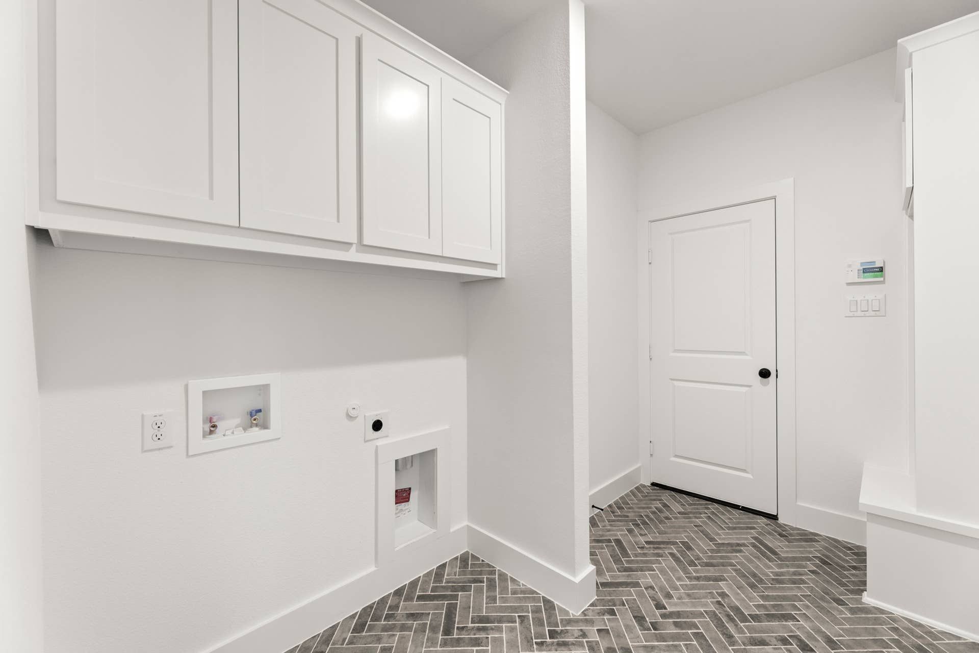 Modern utility room with white cabinets and herringbone tile flooring.