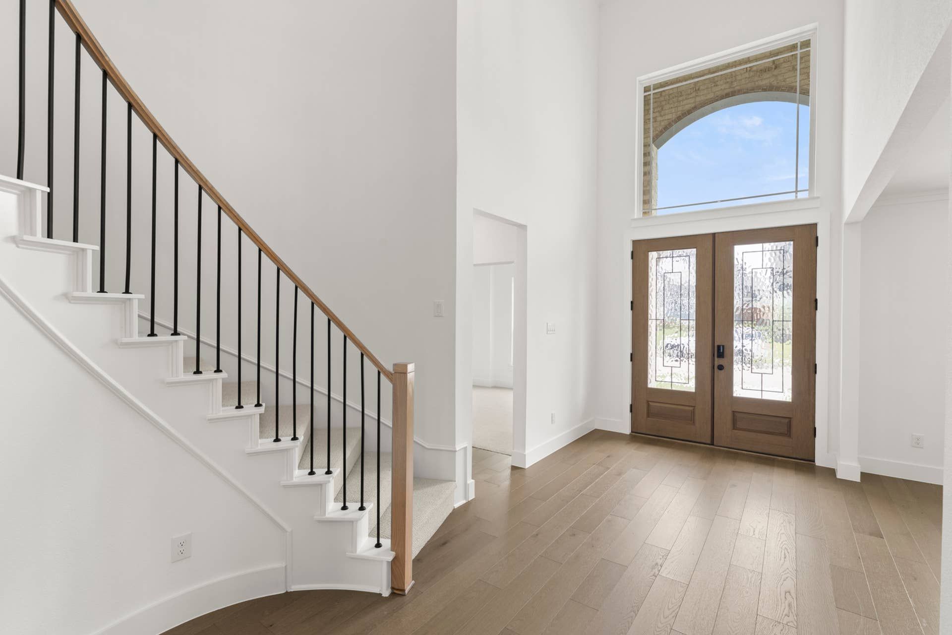 Bright entryway with wooden double doors and elegant curved staircase.
