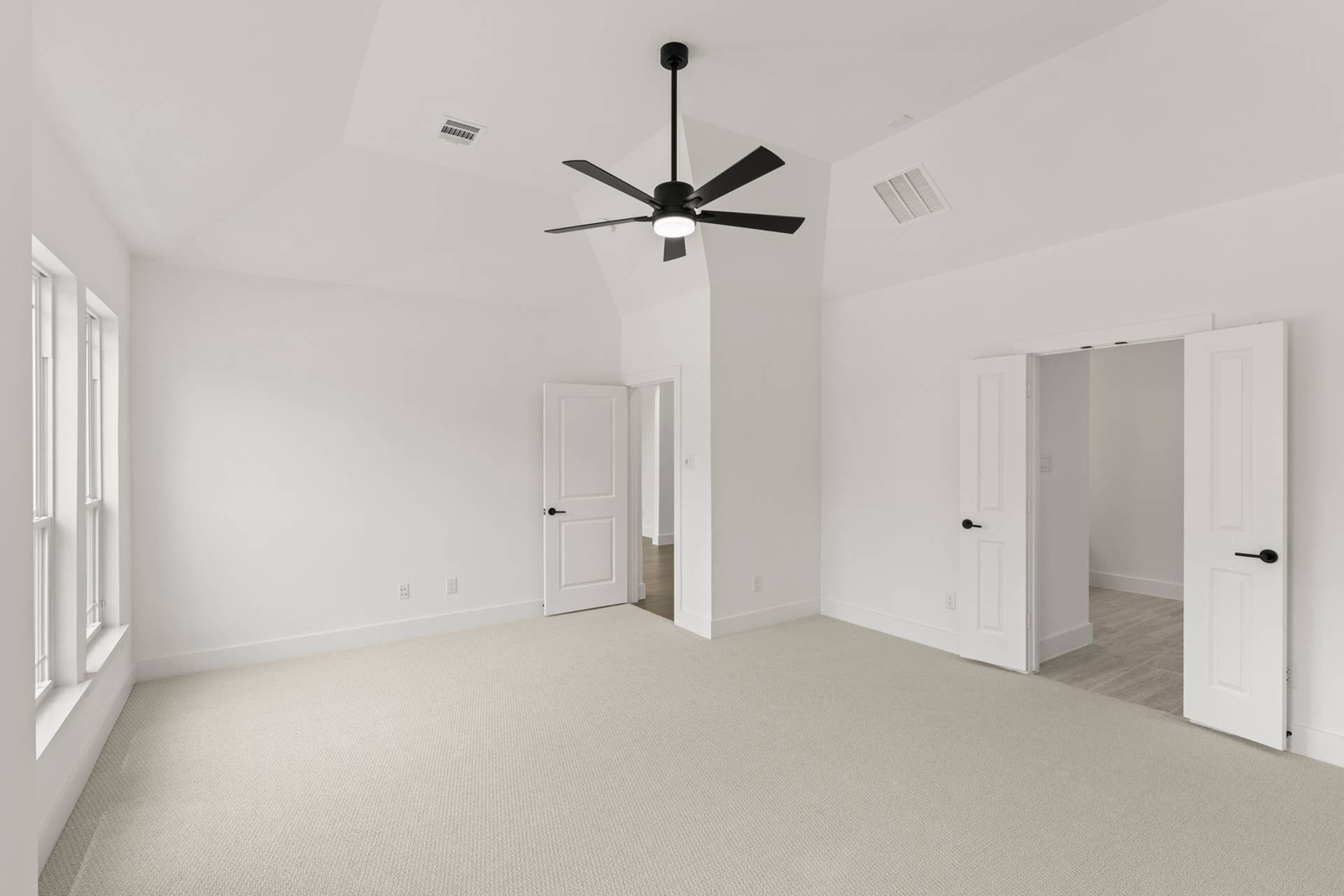 Spacious primary bedroom with ceiling fan and large windows.