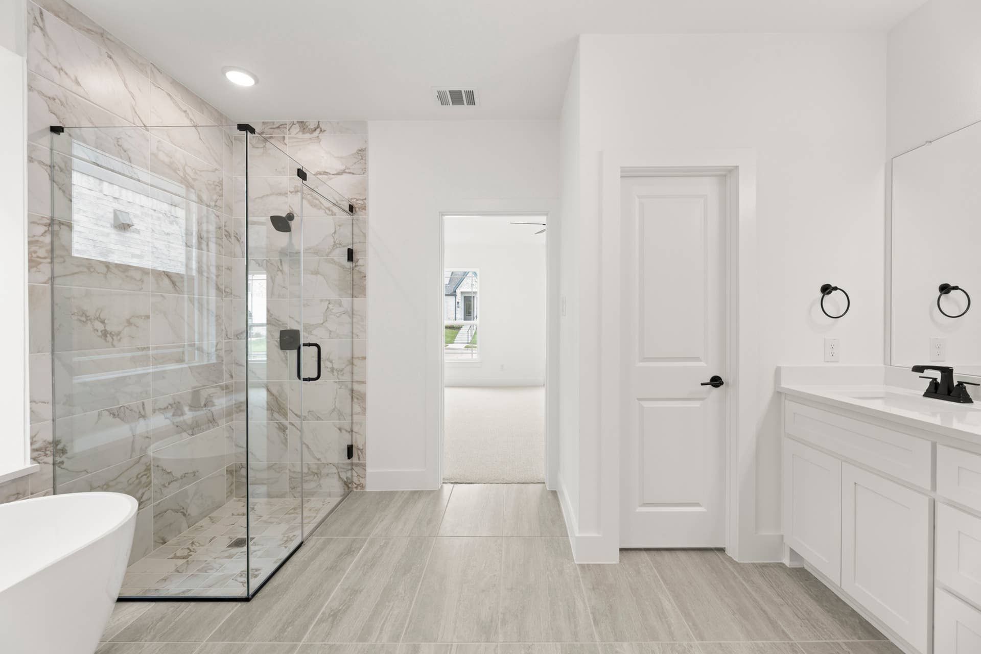 Modern bathroom with glass shower, marble tiles, and freestanding tub.