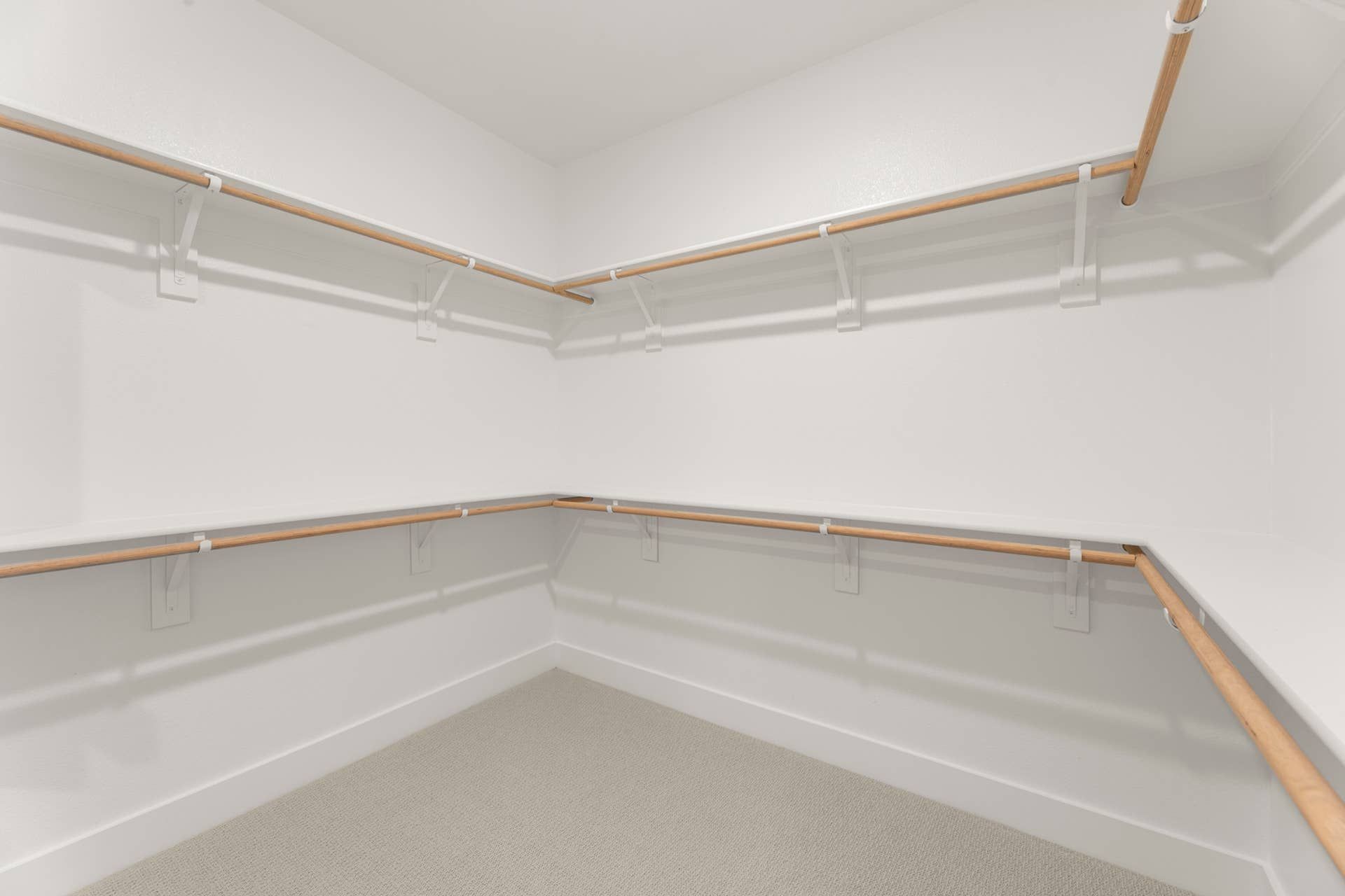 Spacious walk-in closet with wooden rod and white shelving.
