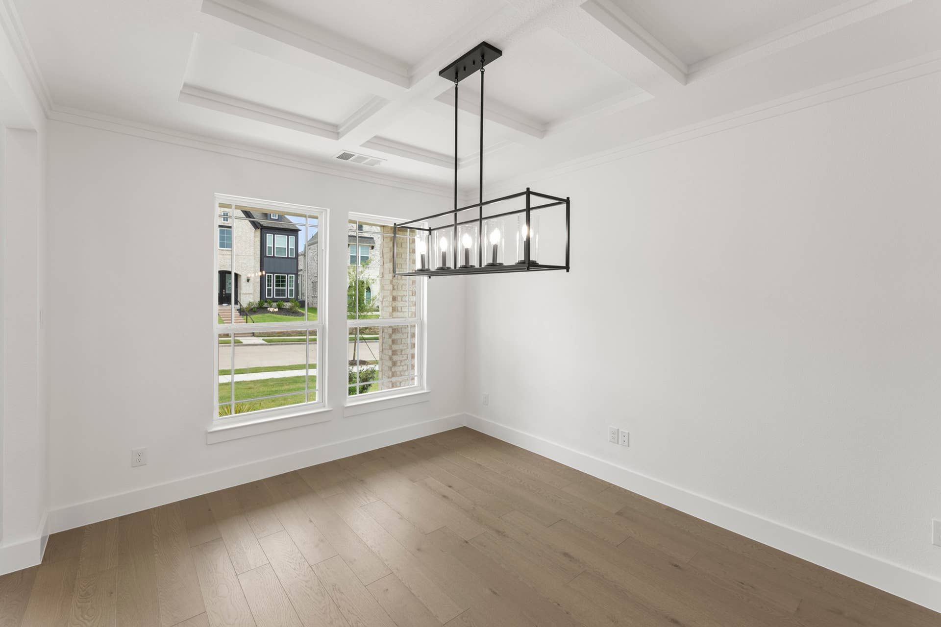 Modern dining room with coffered ceiling and large windows overlooking neighborhood.