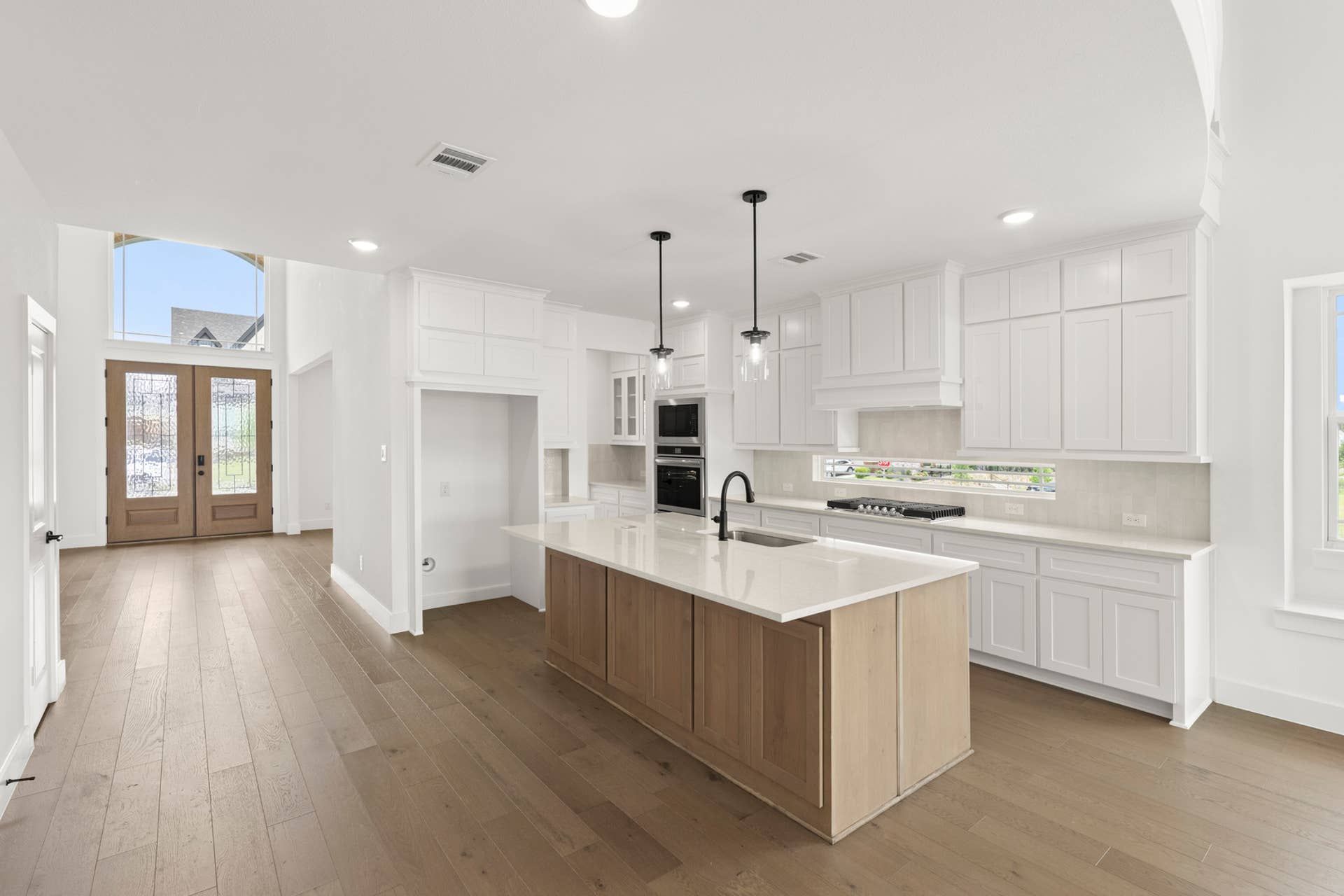 Spacious kitchen interior with white cabinetry and large island, natural light streaming in.