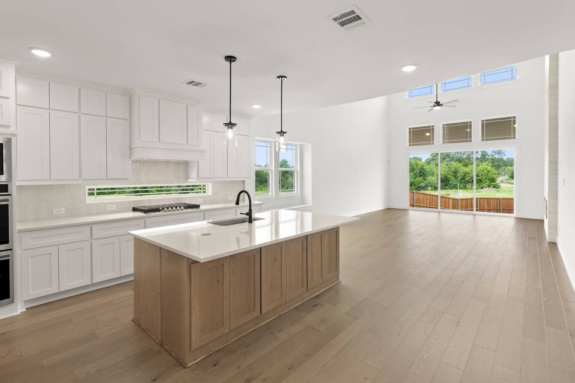 Spacious modern kitchen with island, pendant lights, and large windows overlooking greenery.