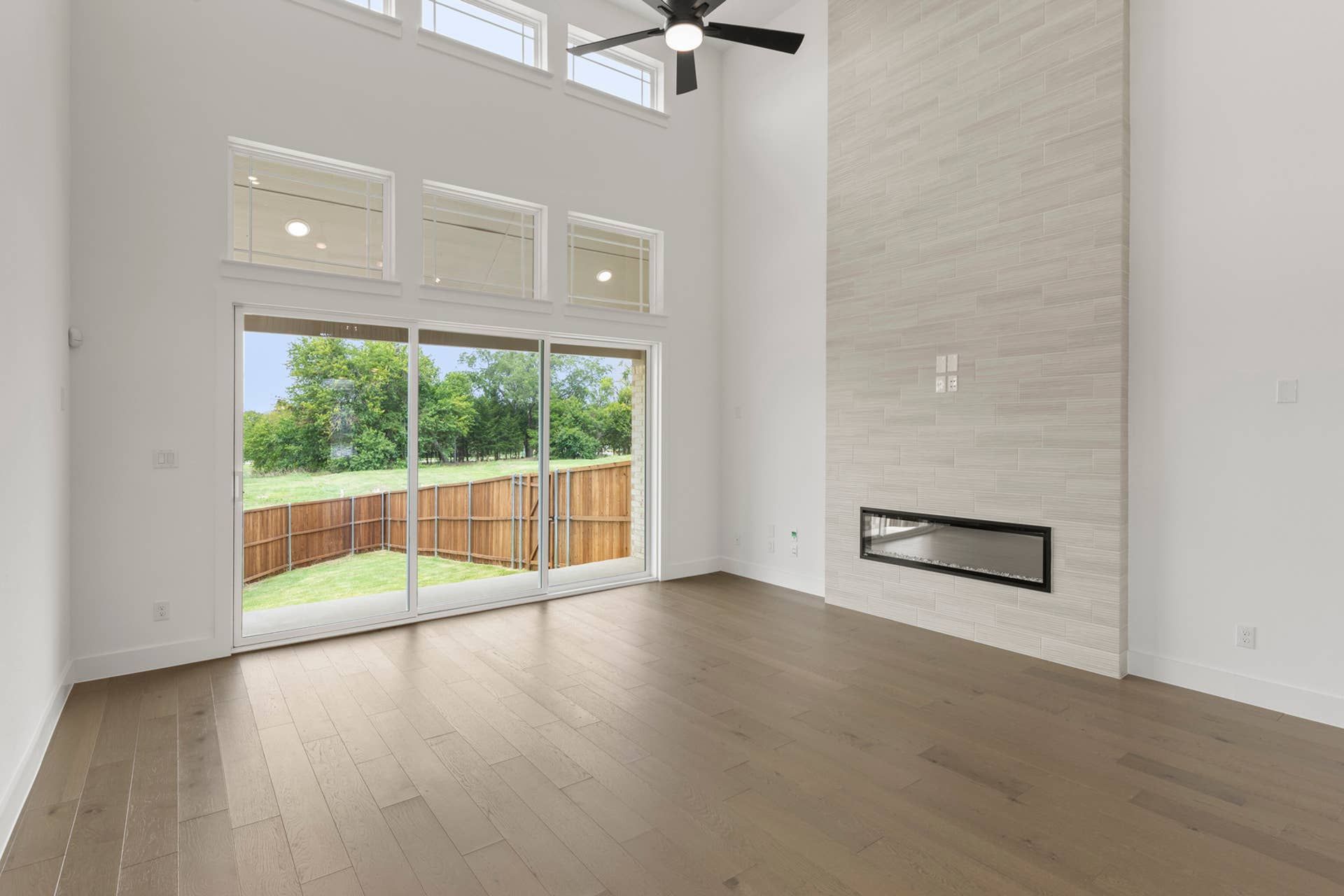 Spacious living room with high ceiling, modern fireplace, and large sliding glass doors.