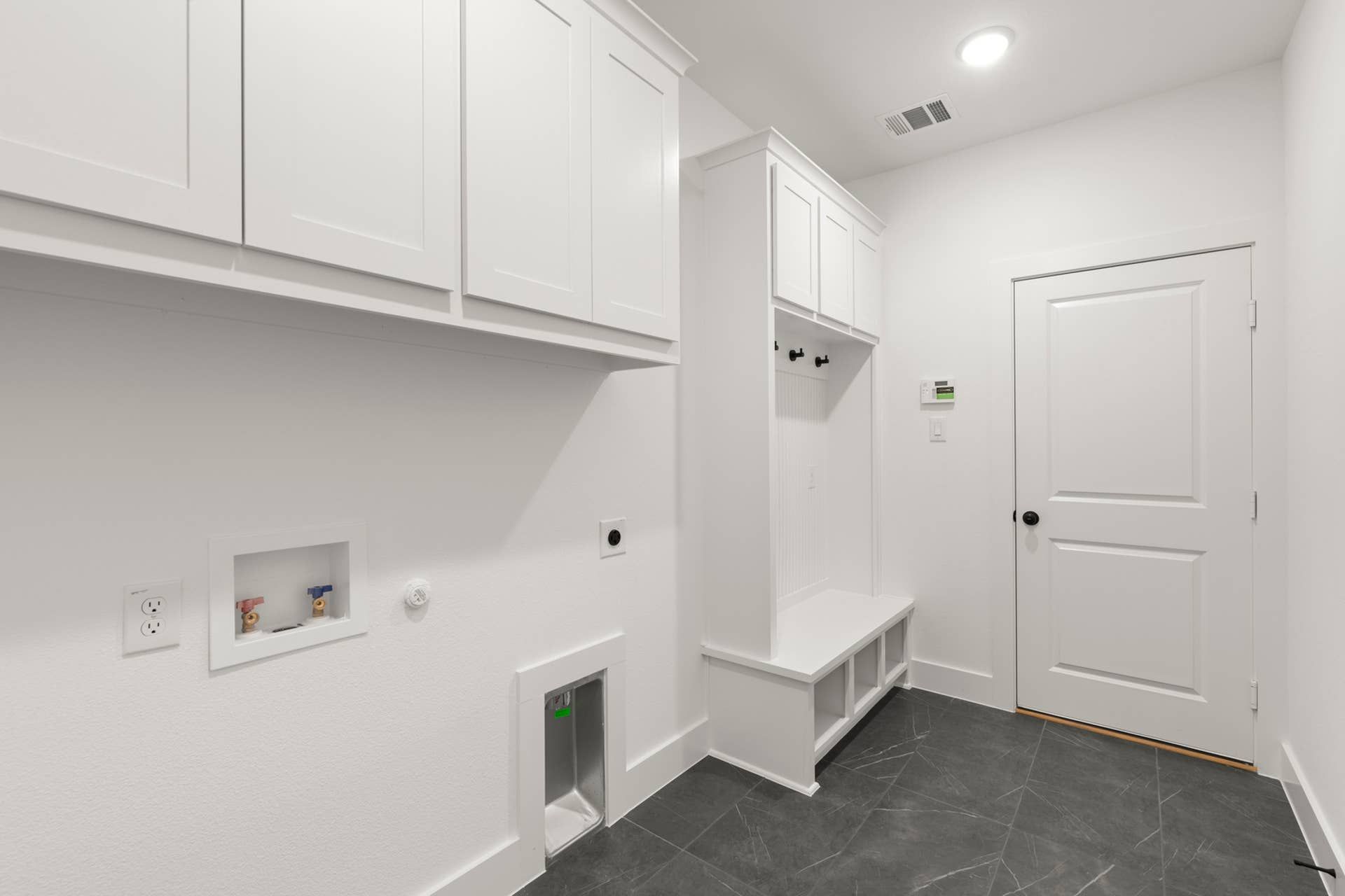 Modern utility room with white cabinetry and black tile flooring.