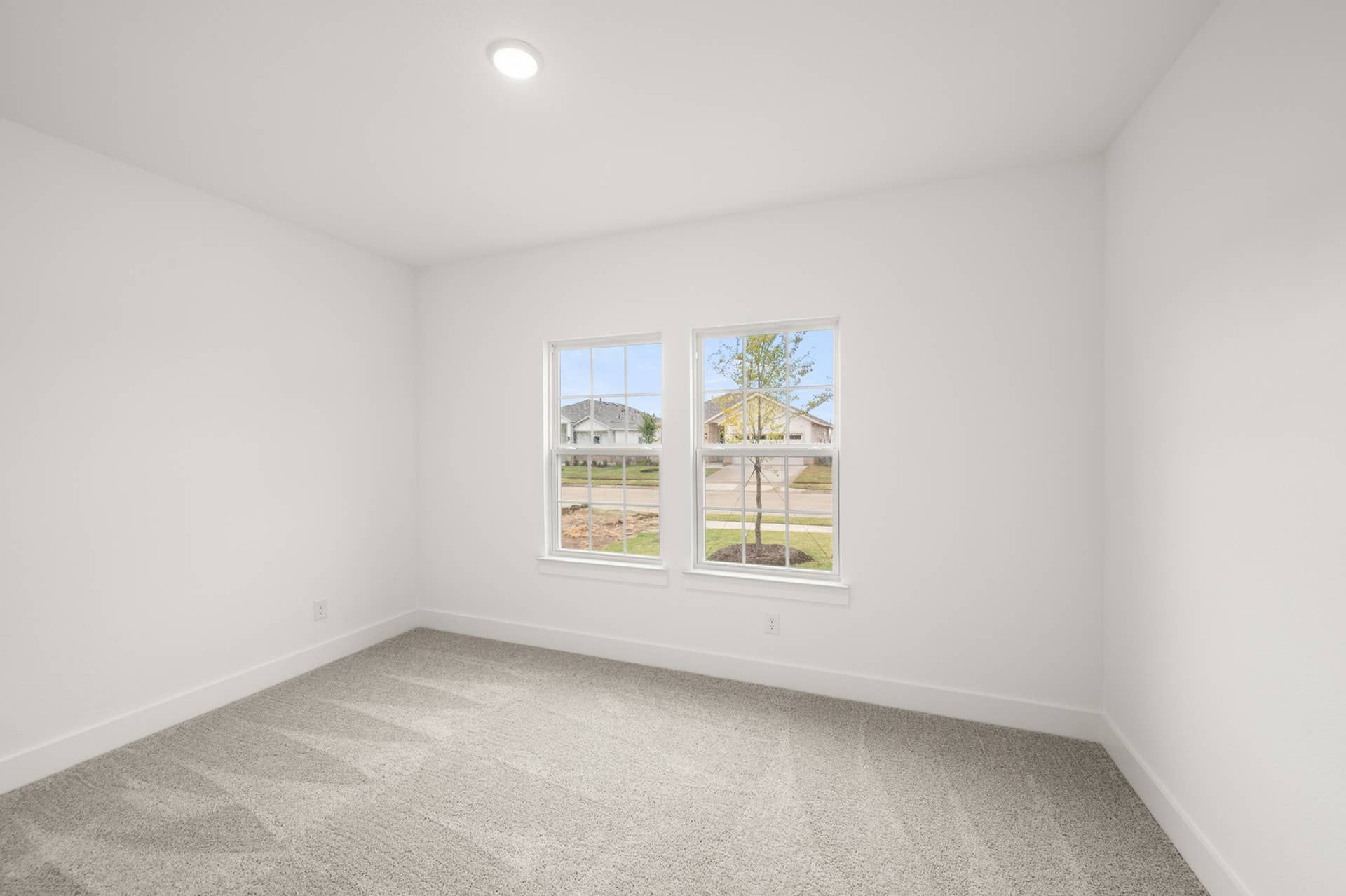 Bright bedroom with neutral carpeting and double windows overlooking the street.