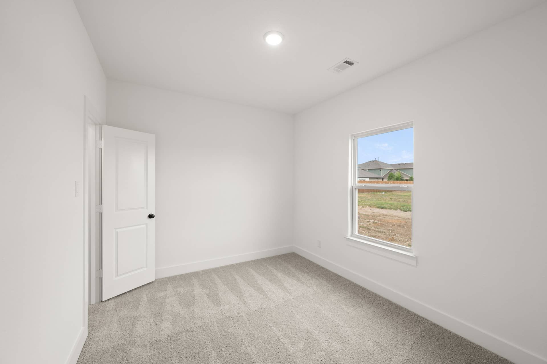 Bright, empty bedroom with carpet and single window overlooking a suburban street.