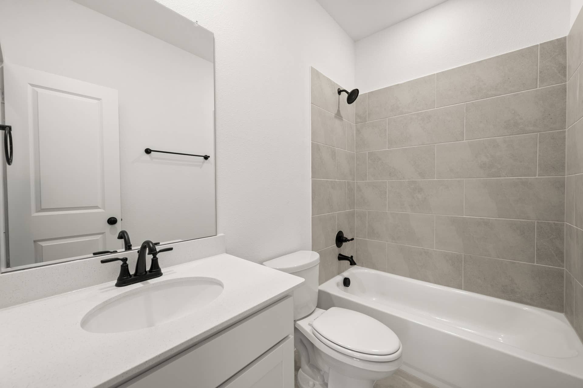 Modern bathroom with white vanity, black fixtures, and tiled bathtub.