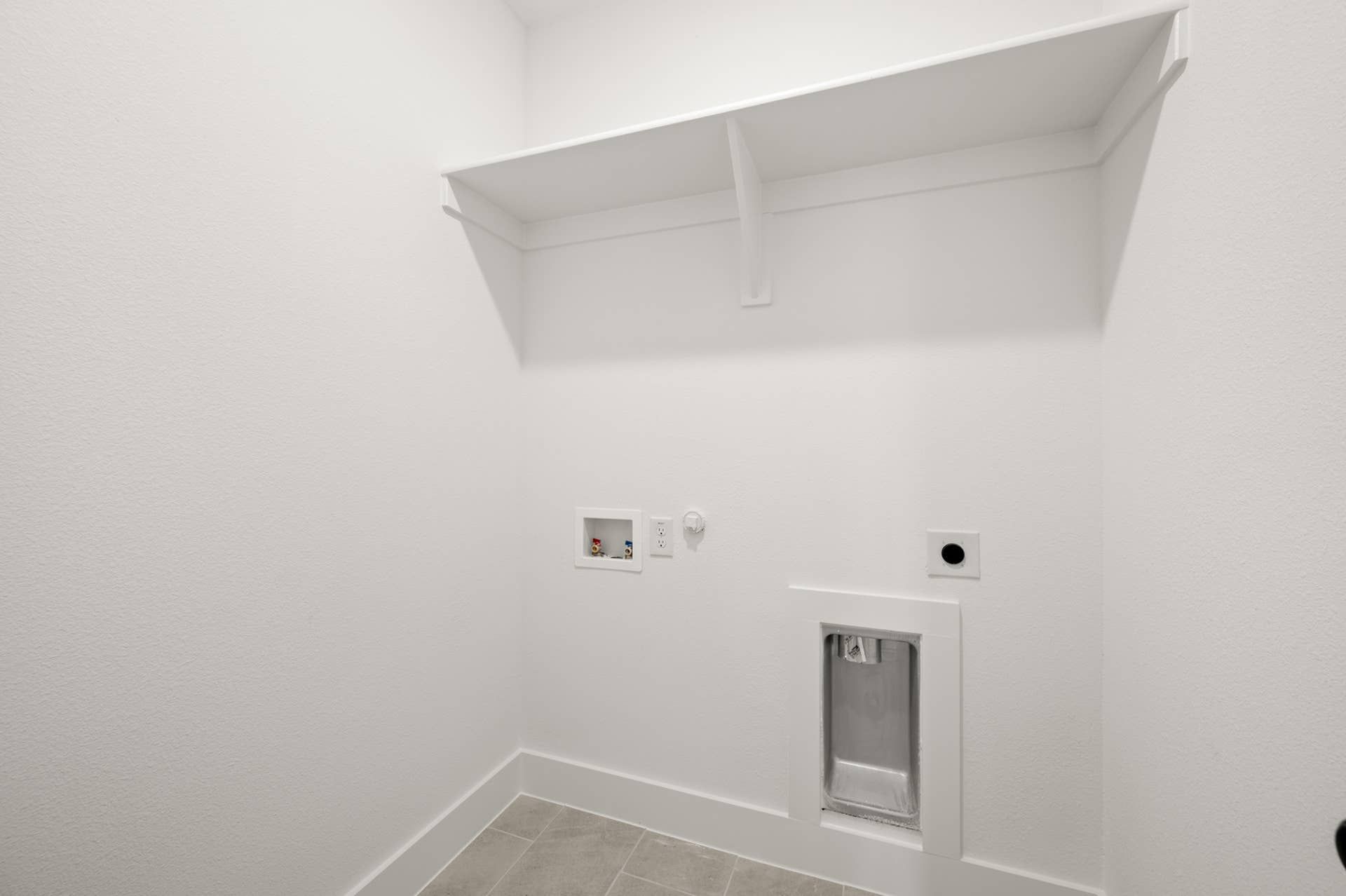 Minimalist white utility room with shelving and plumbing connections.