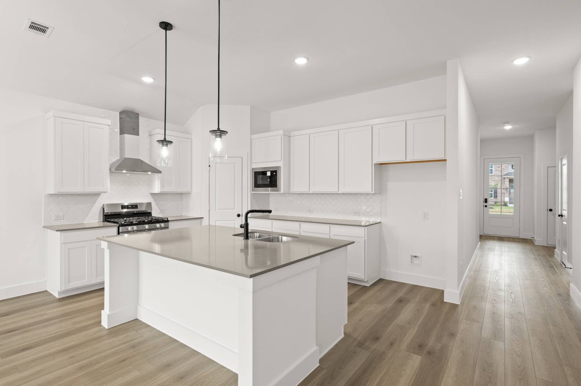 Modern kitchen with white cabinetry, island, pendant lighting, and stainless steel appliances.