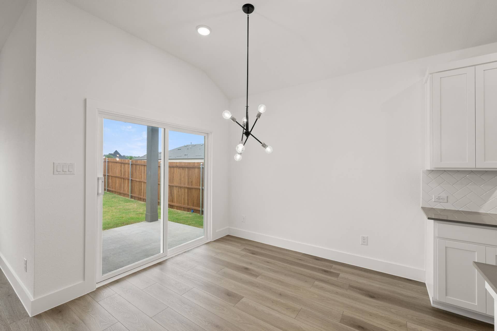 Modern dining area with sliding glass door, wood flooring, and geometric light fixture.
