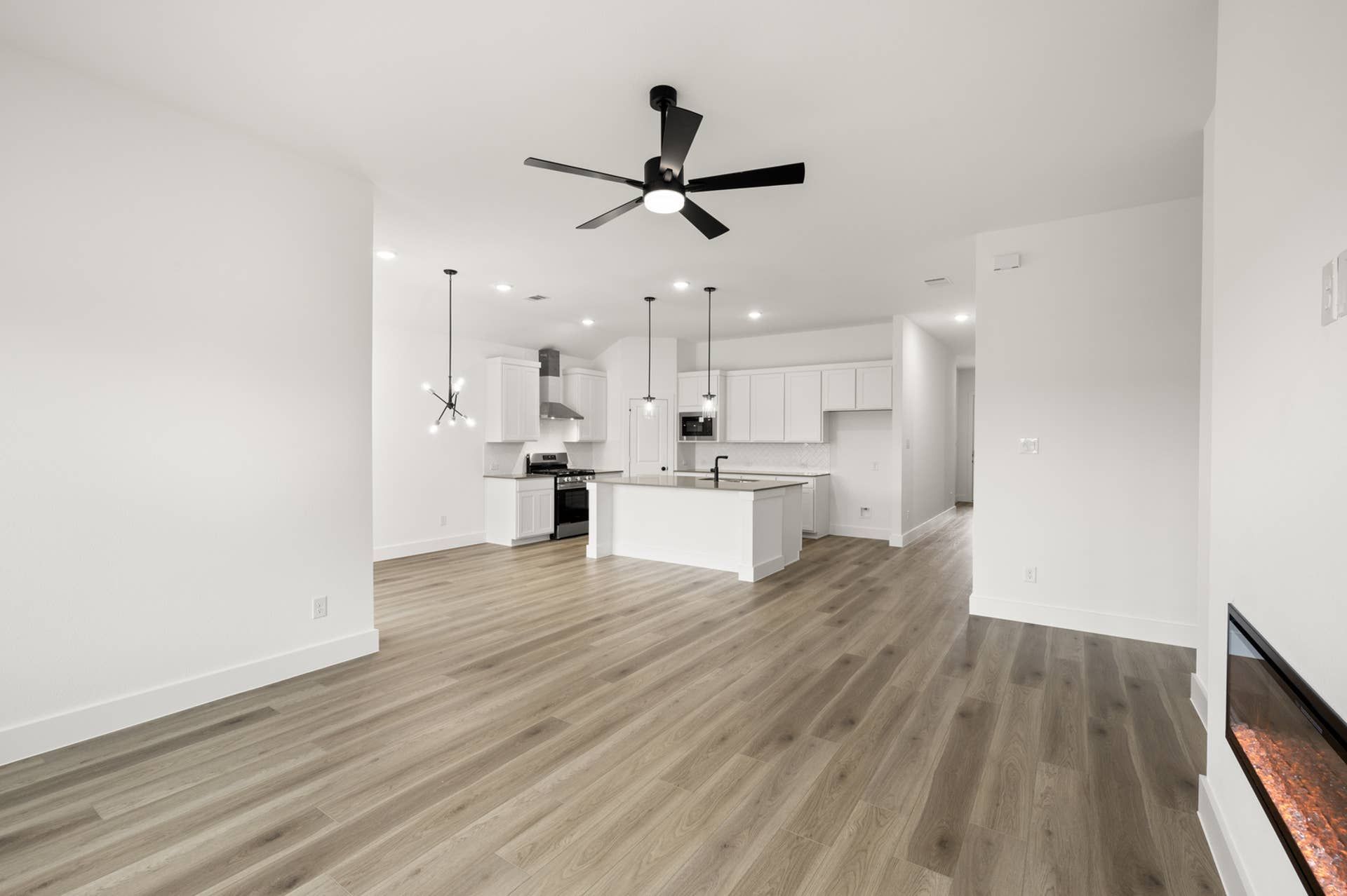 Modern living room with open kitchen, wood flooring, and sleek ceiling fan.