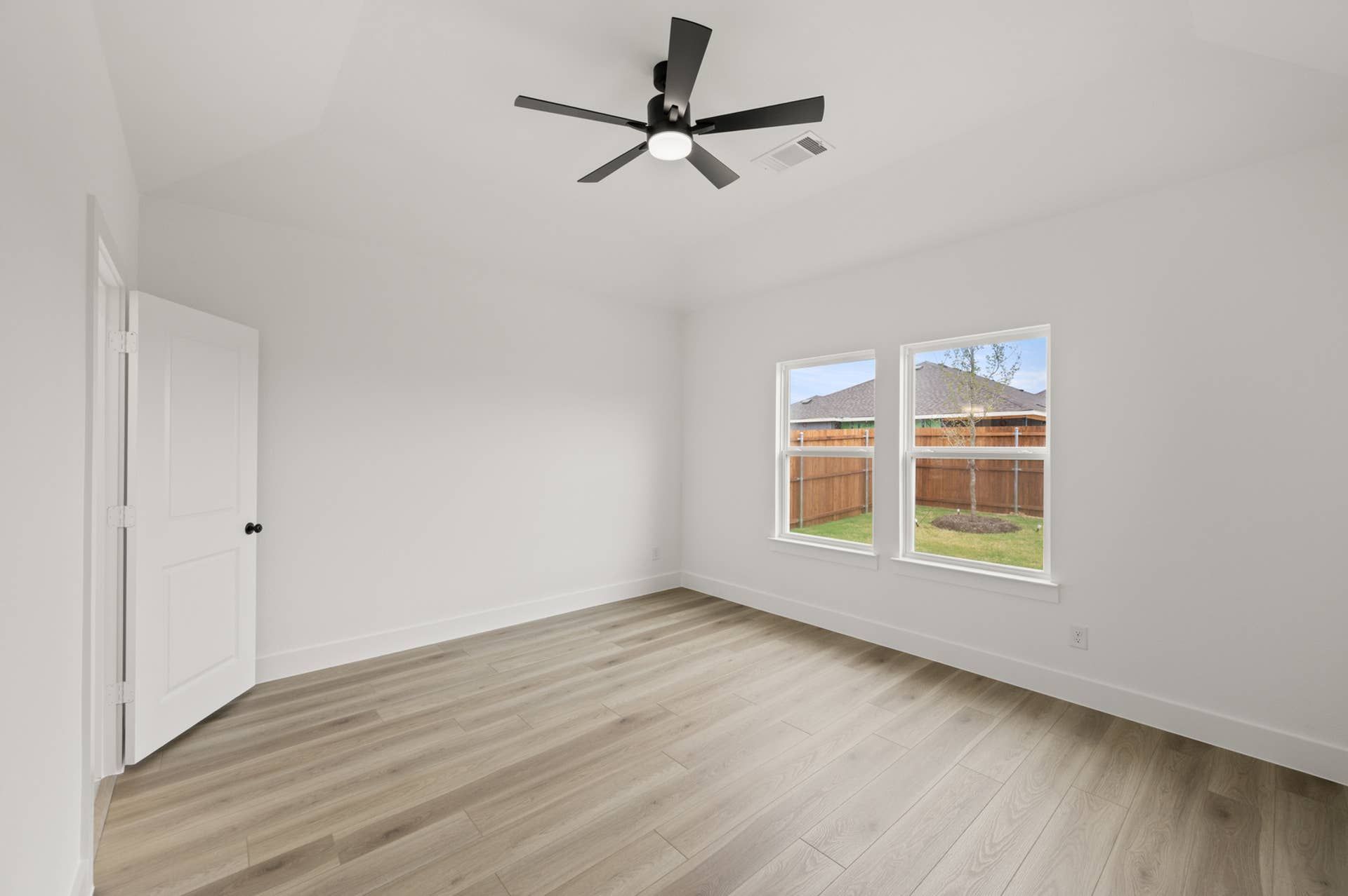 Bright primary suite with wood flooring and ceiling fan, overlooking fenced yard.