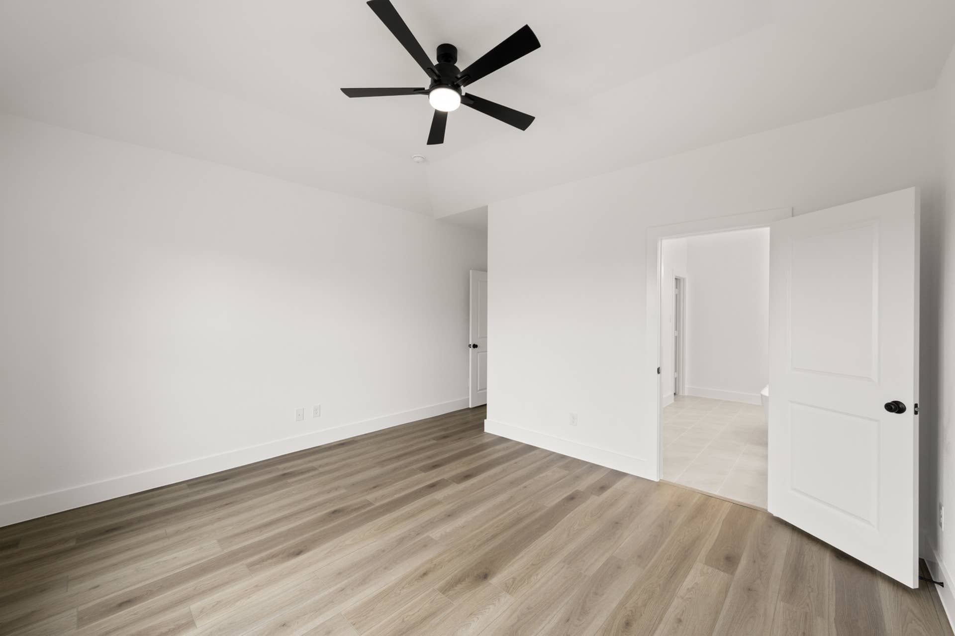 Spacious primary suite with wood flooring and ceiling fan.