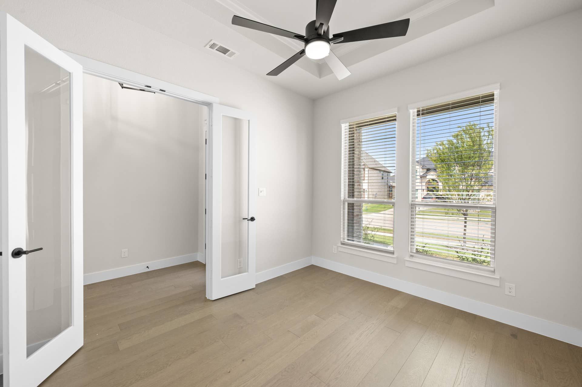 Bright study room with glass French doors and large windows overlooking the street.