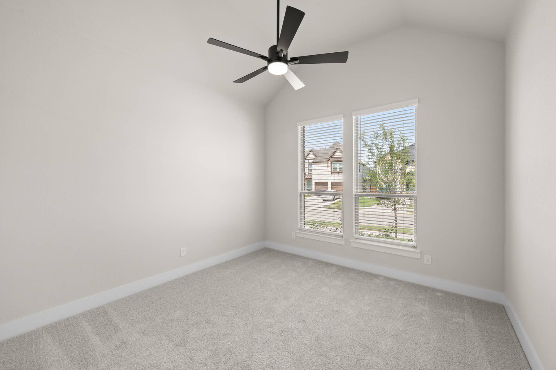 Bright bedroom with gray carpet, ceiling fan, and large windows with blinds.