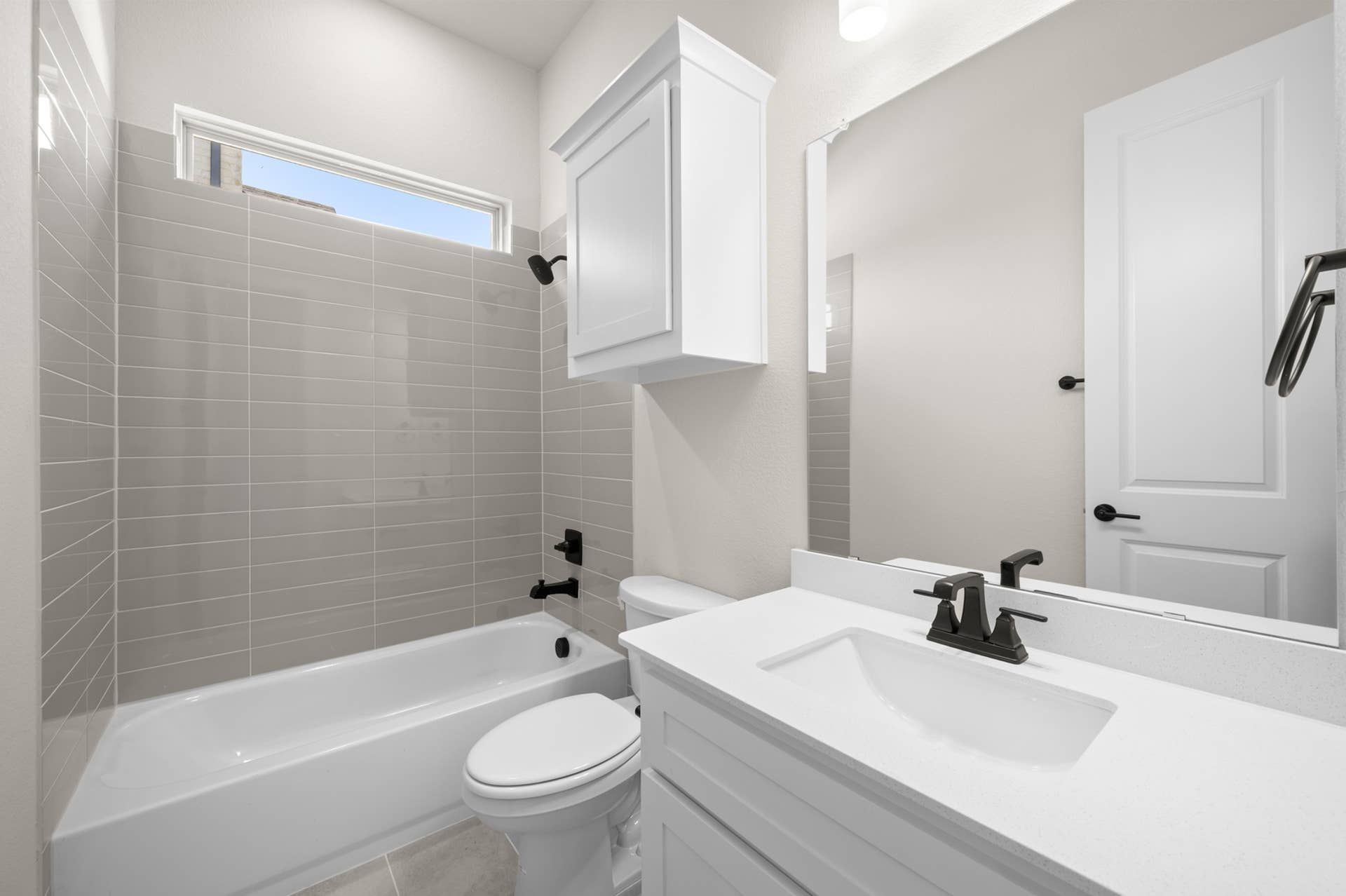 Modern bathroom with sleek fixtures, white cabinetry, and gray tiled bathtub surround.