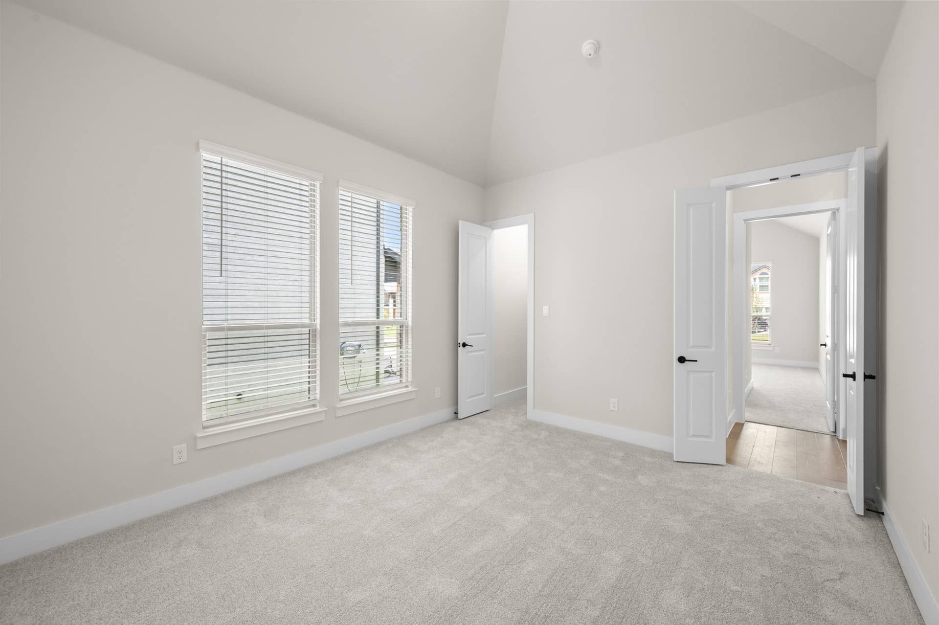 Bright, empty bedroom with large windows and plush carpeting.