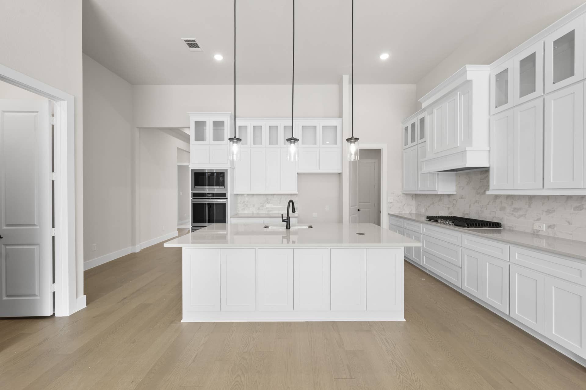 Modern kitchen with white cabinetry, island, pendant lighting, and hardwood floors.