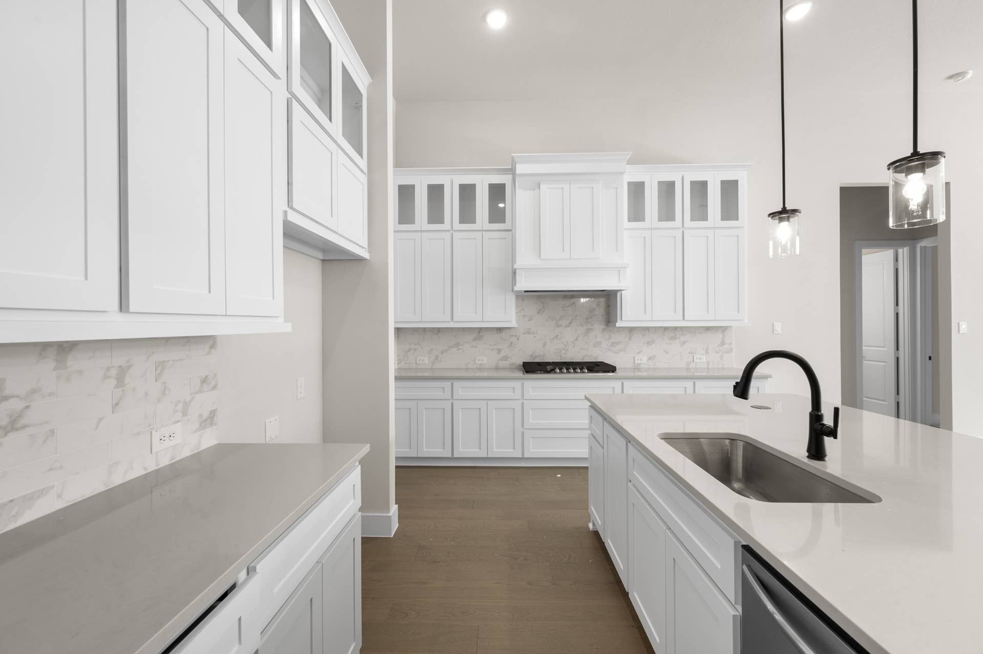 Modern kitchen with white cabinetry, marble backsplash, and large island sink.