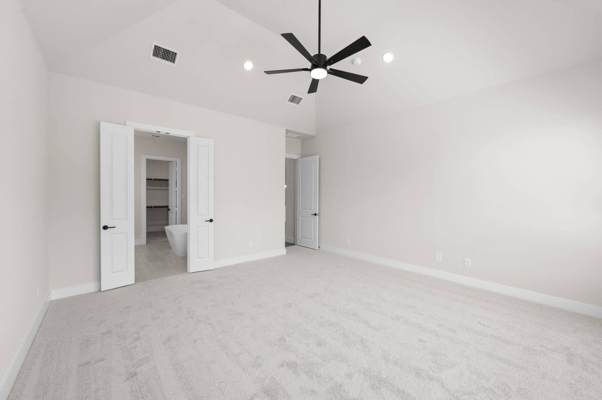 Spacious primary suite with vaulted ceiling, modern fan, and ensuite bathroom entrance.