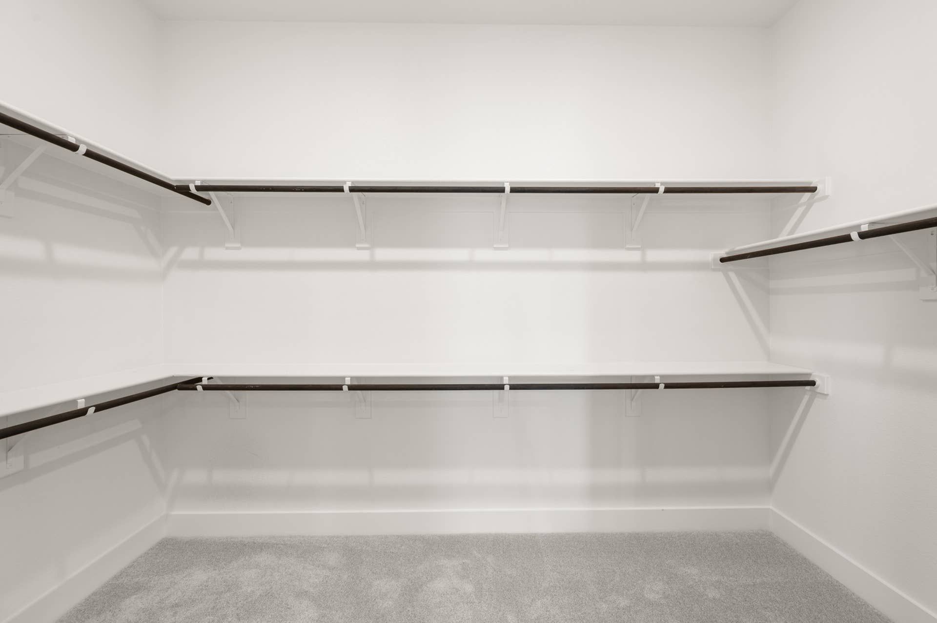 Spacious walk-in closet with multiple dark wood hanging rods and white shelves.