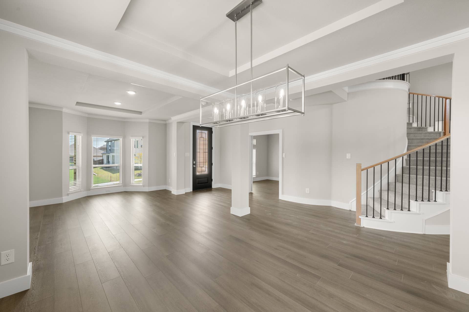 Spacious interior with hardwood floors, modern chandelier, and curved staircase.