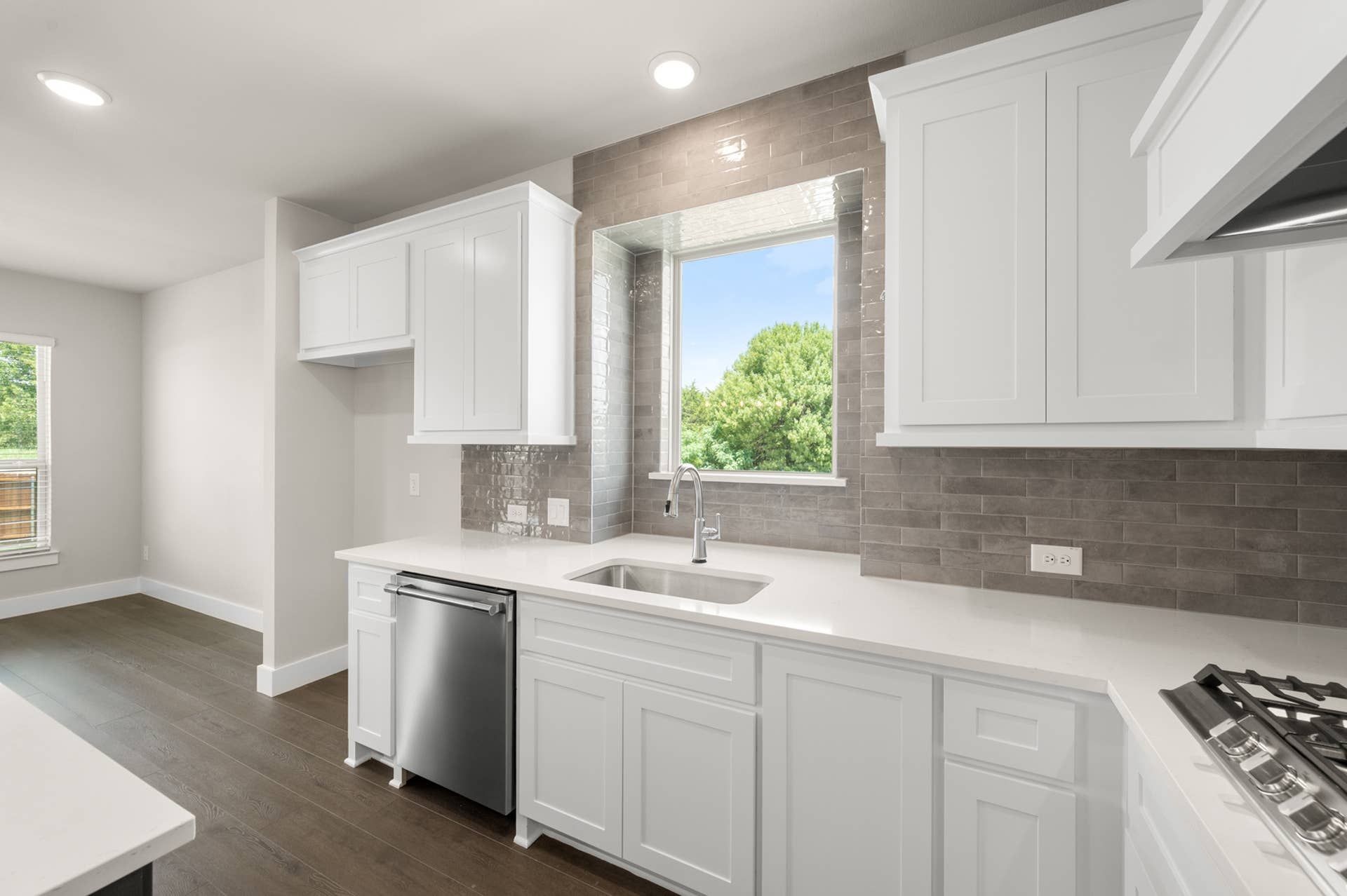 Modern kitchen with white cabinets, gray backsplash, and stainless steel appliances.