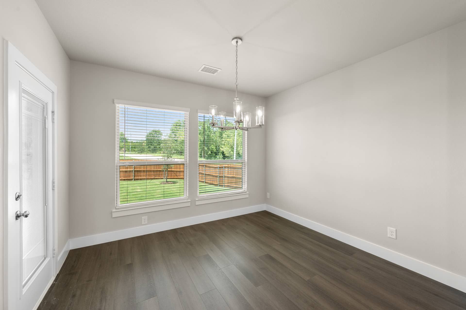 Modern dining room with large windows, hardwood floor, and elegant chandelier.