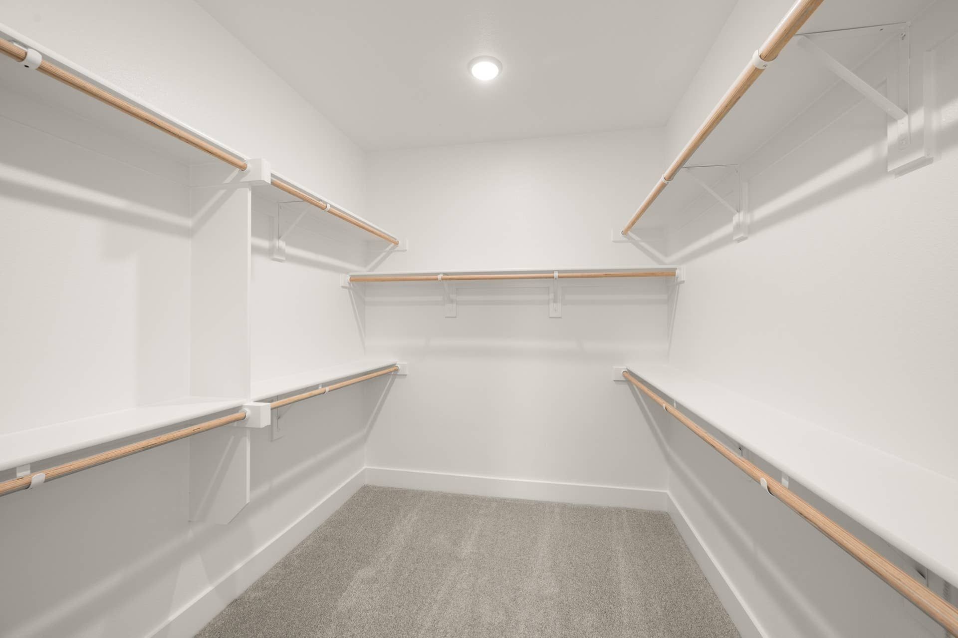 Spacious walk-in closet with multiple wooden hanging rods and carpeted flooring.
