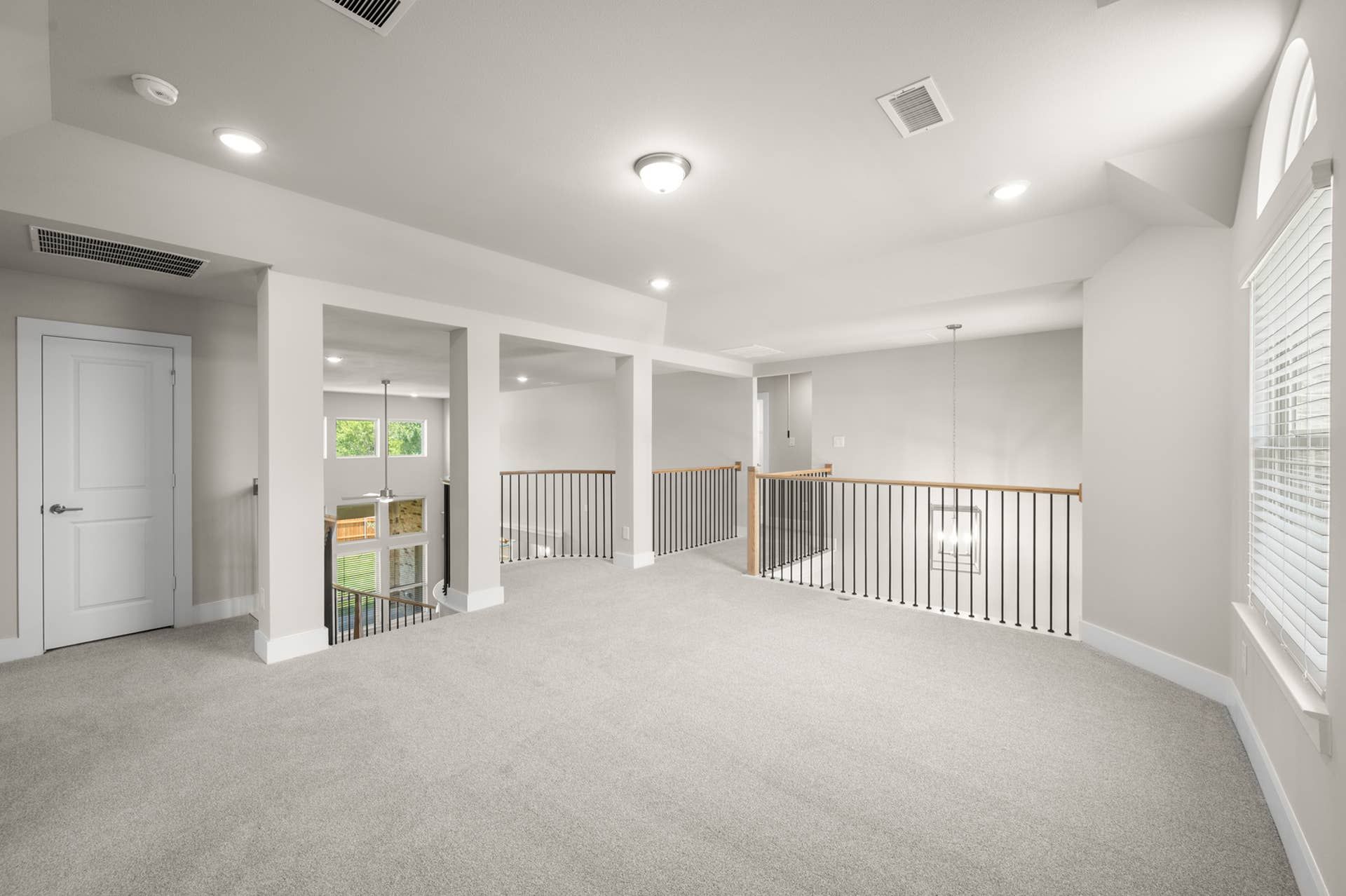 Spacious game room with carpeted flooring and modern railing overlooking lower level.