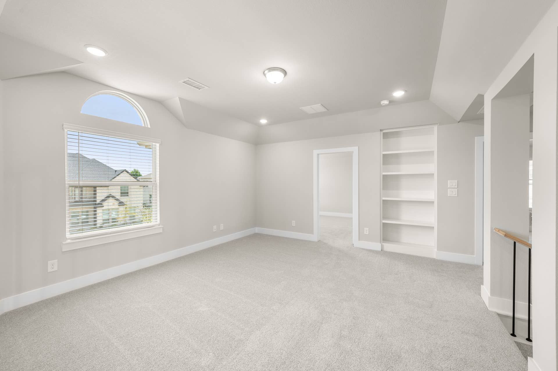 Spacious game room with carpet, built-in shelving, and arched window.