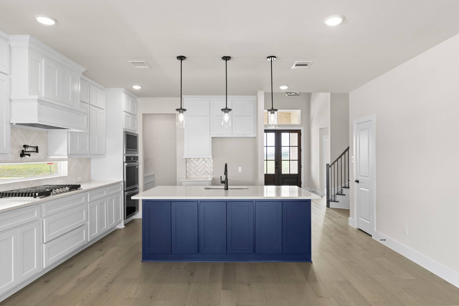 Modern kitchen with blue island, white cabinets, pendant lights, and hardwood floors.