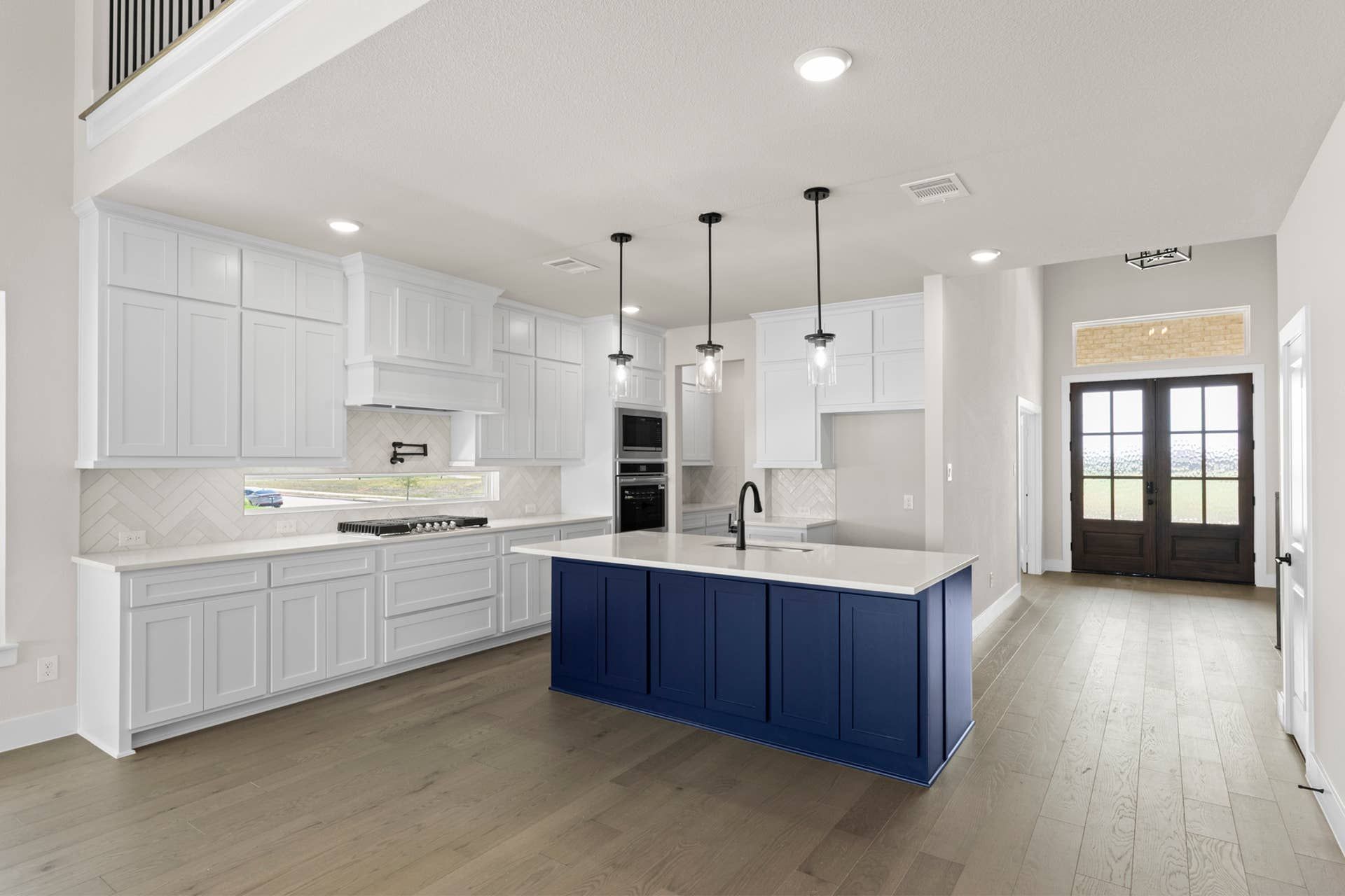 Modern kitchen with white cabinets, blue island, and pendant lighting.