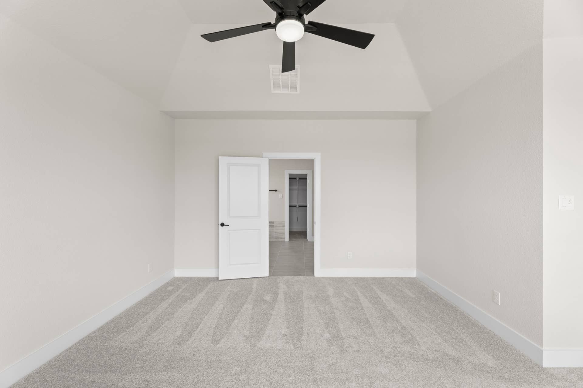 Spacious bedroom with vaulted ceiling, ceiling fan, and plush carpet.