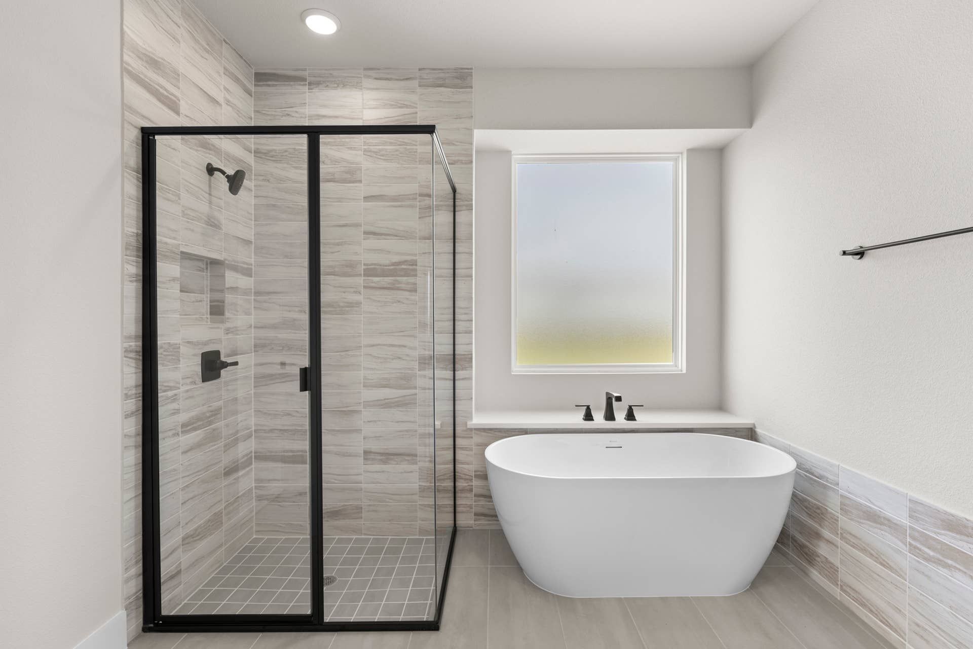 Modern bathroom with glass shower and freestanding tub beside frosted window.