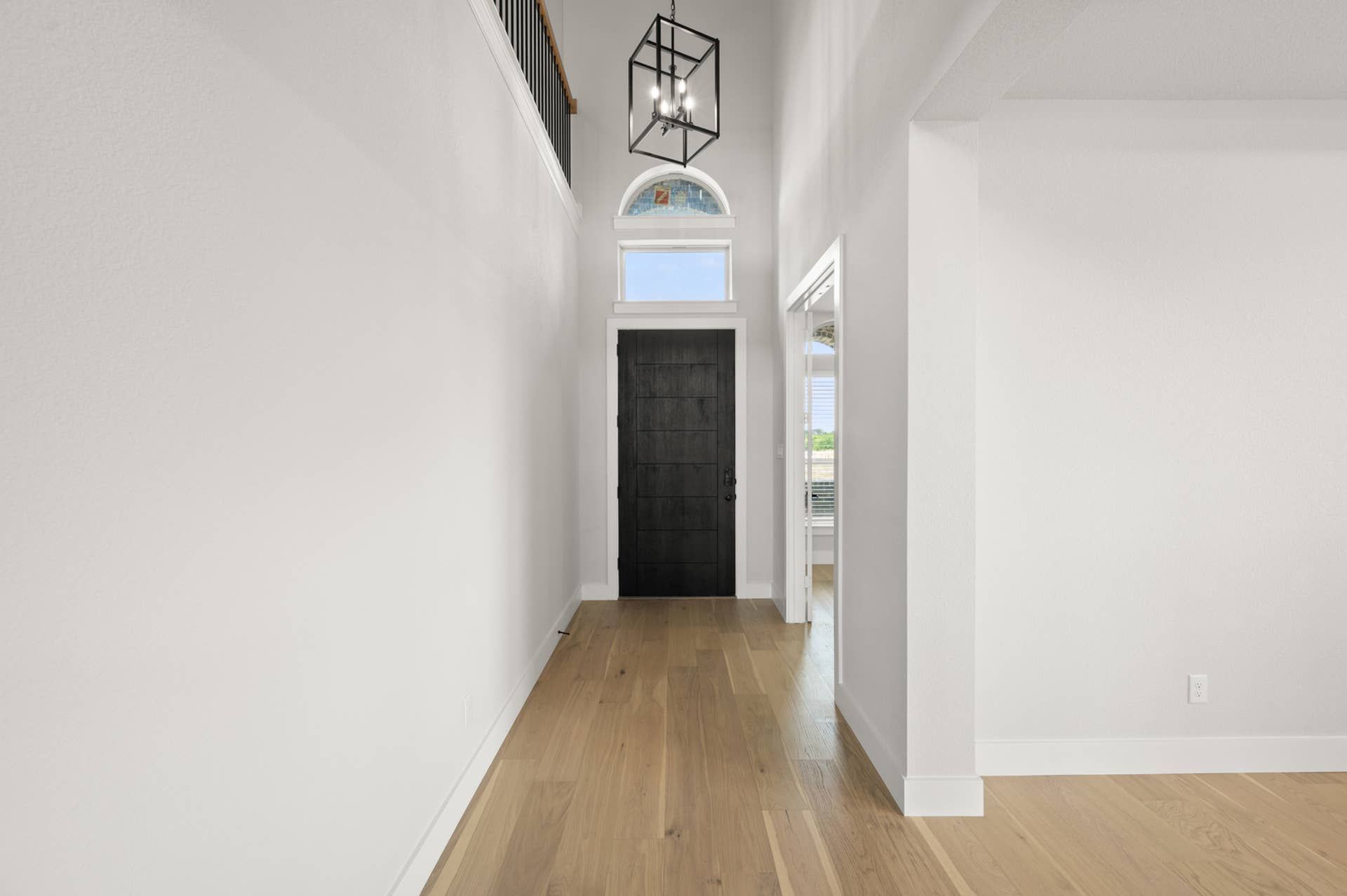 Bright entryway with high ceiling, dark door, and modern chandelier.
