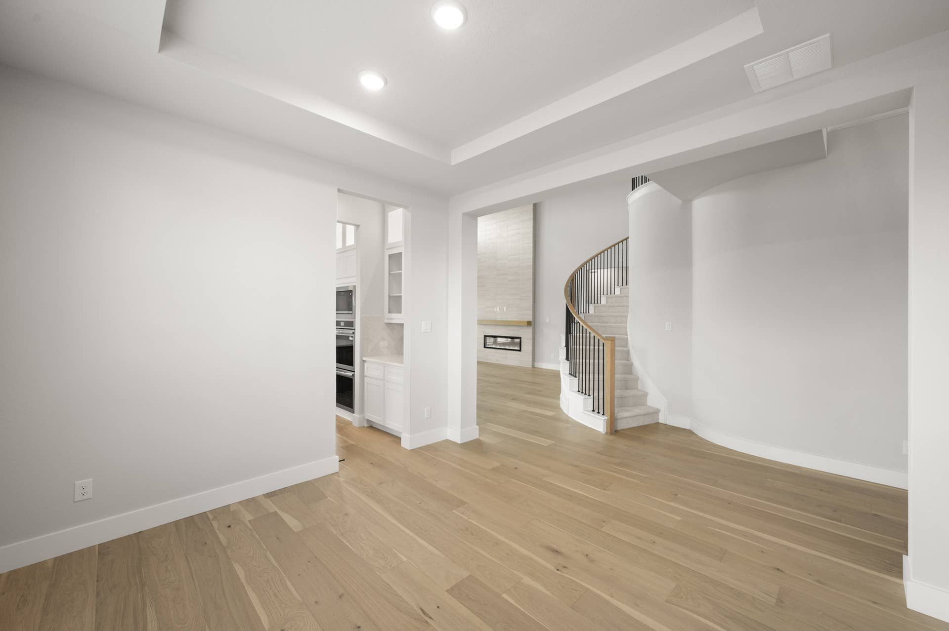 Spacious interior with wooden floors, modern kitchen, and elegant spiral staircase.